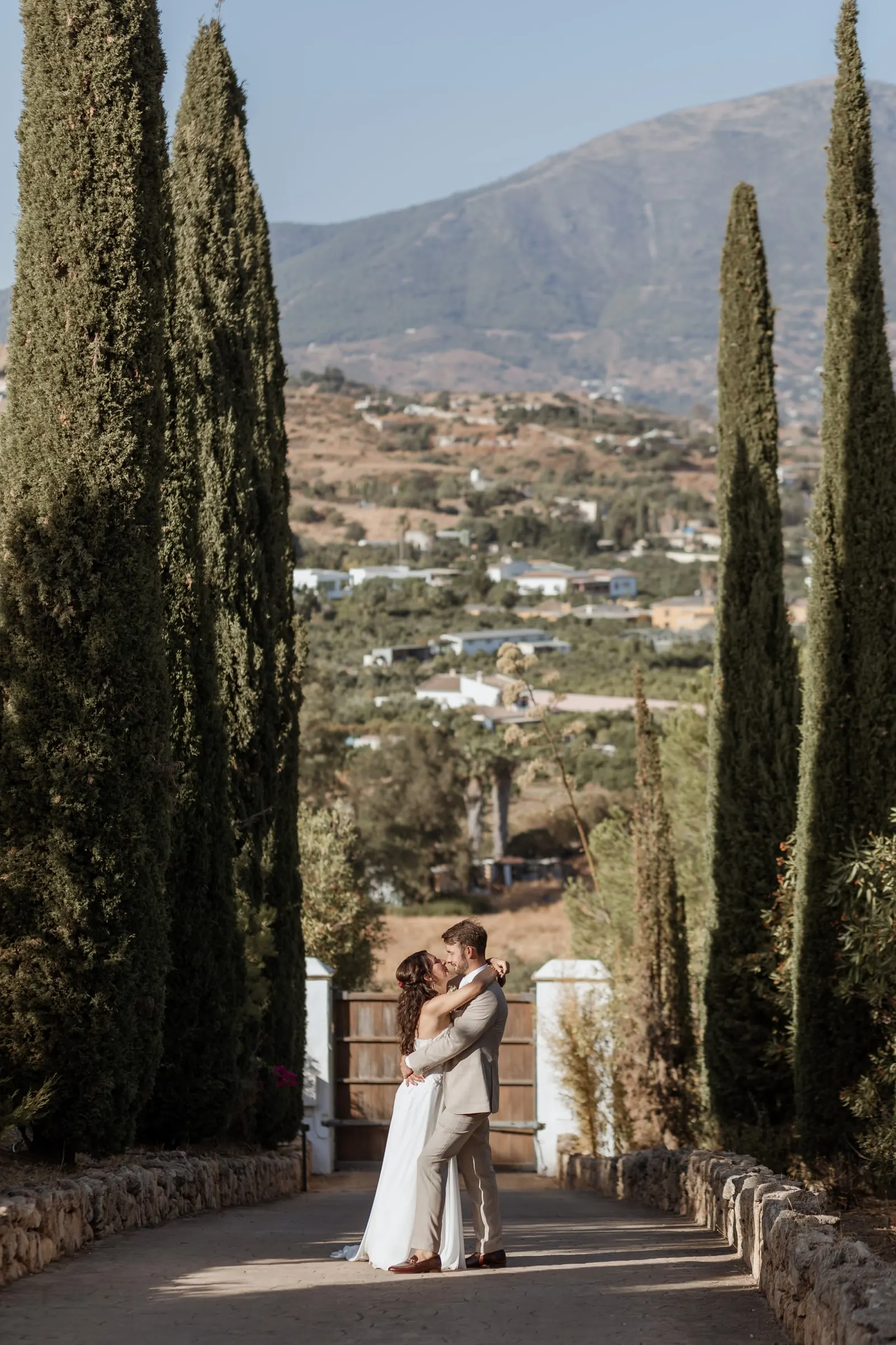 Los novios abrazados al final de una avenida de cipreses con el valle detrás, Hacienda San José, Mijas