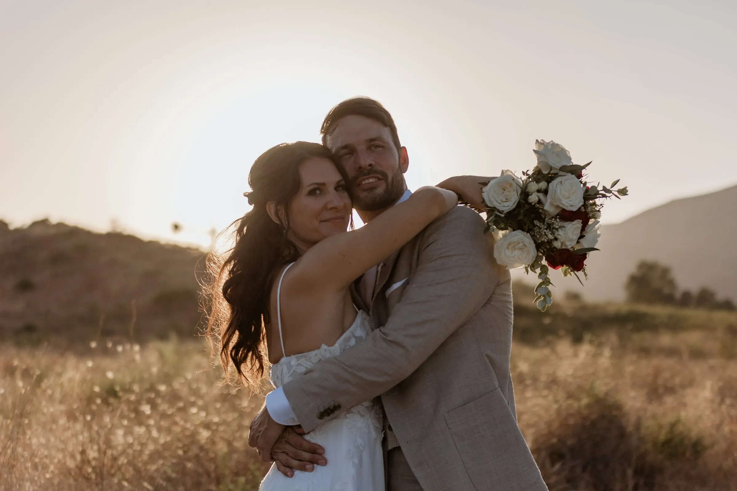 Los novios se abrazan y sonríen a cámara en un campo seco al atardecer, Hacienda San José, Mijas