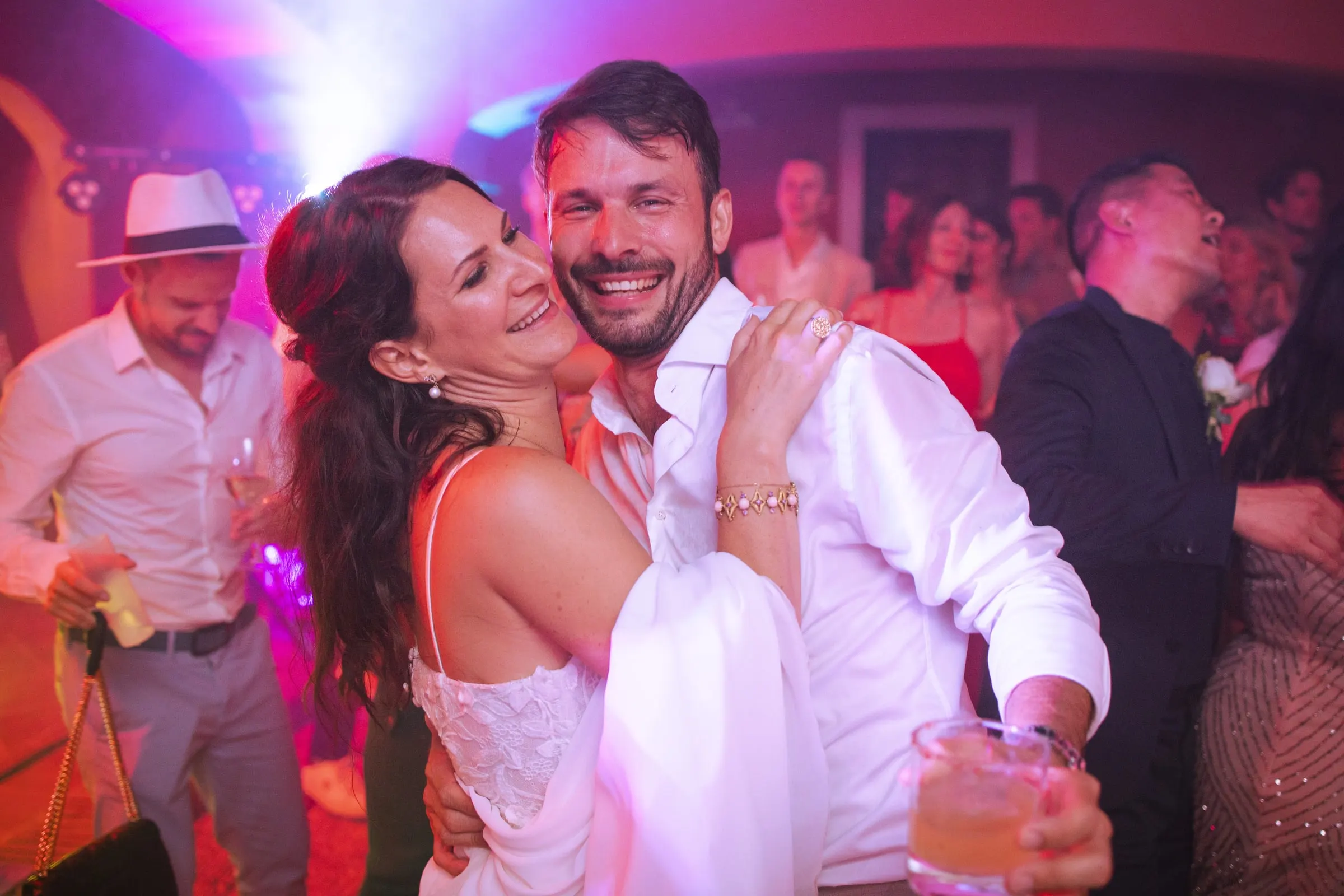 Los novios se abrazan sonrientes en la pista de baile bajo luces rosas, Hacienda San José, Mijas
