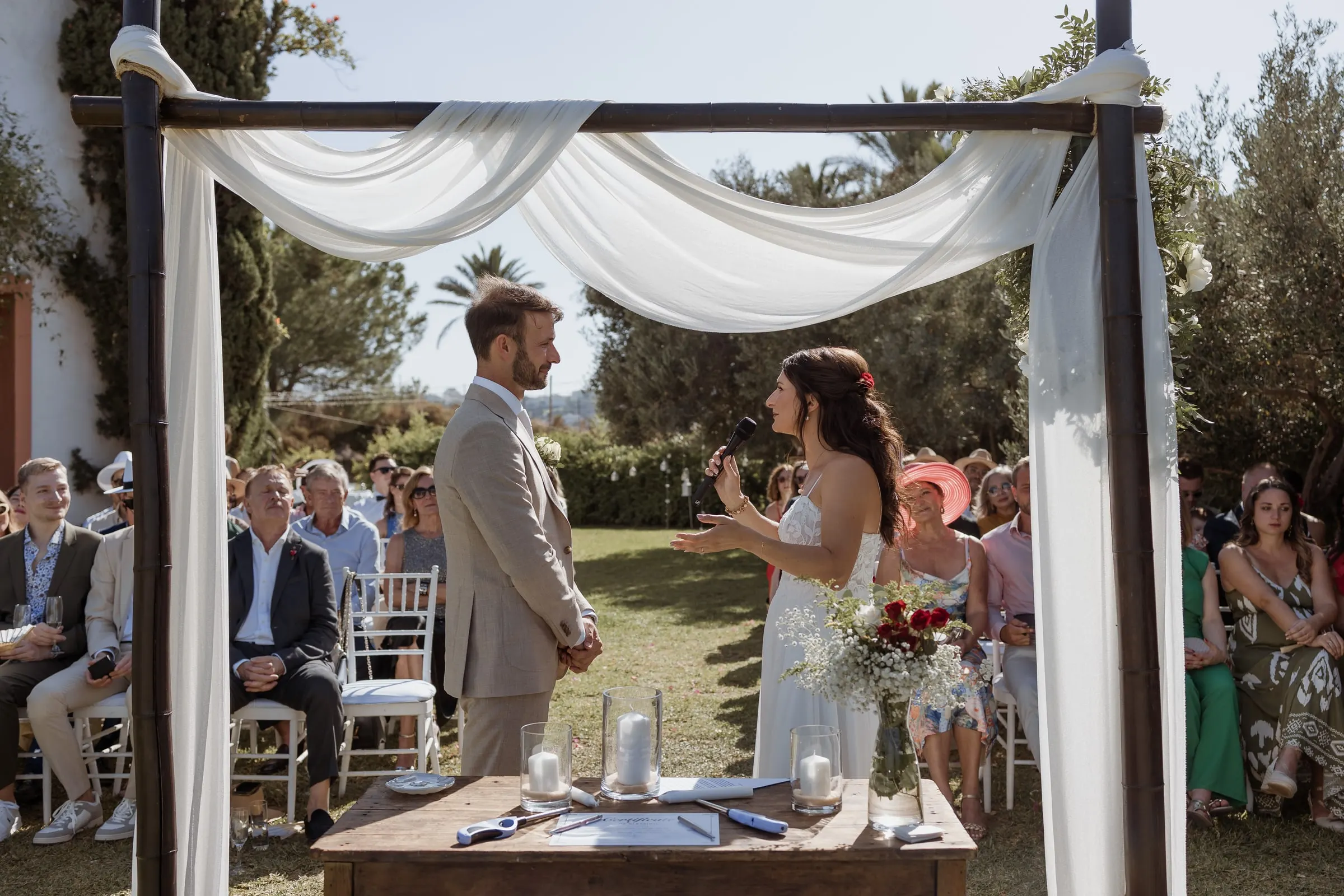 La novia lee sus votos al novio bajo un dosel de tela blanca en el jardín, Hacienda San José, Mijas