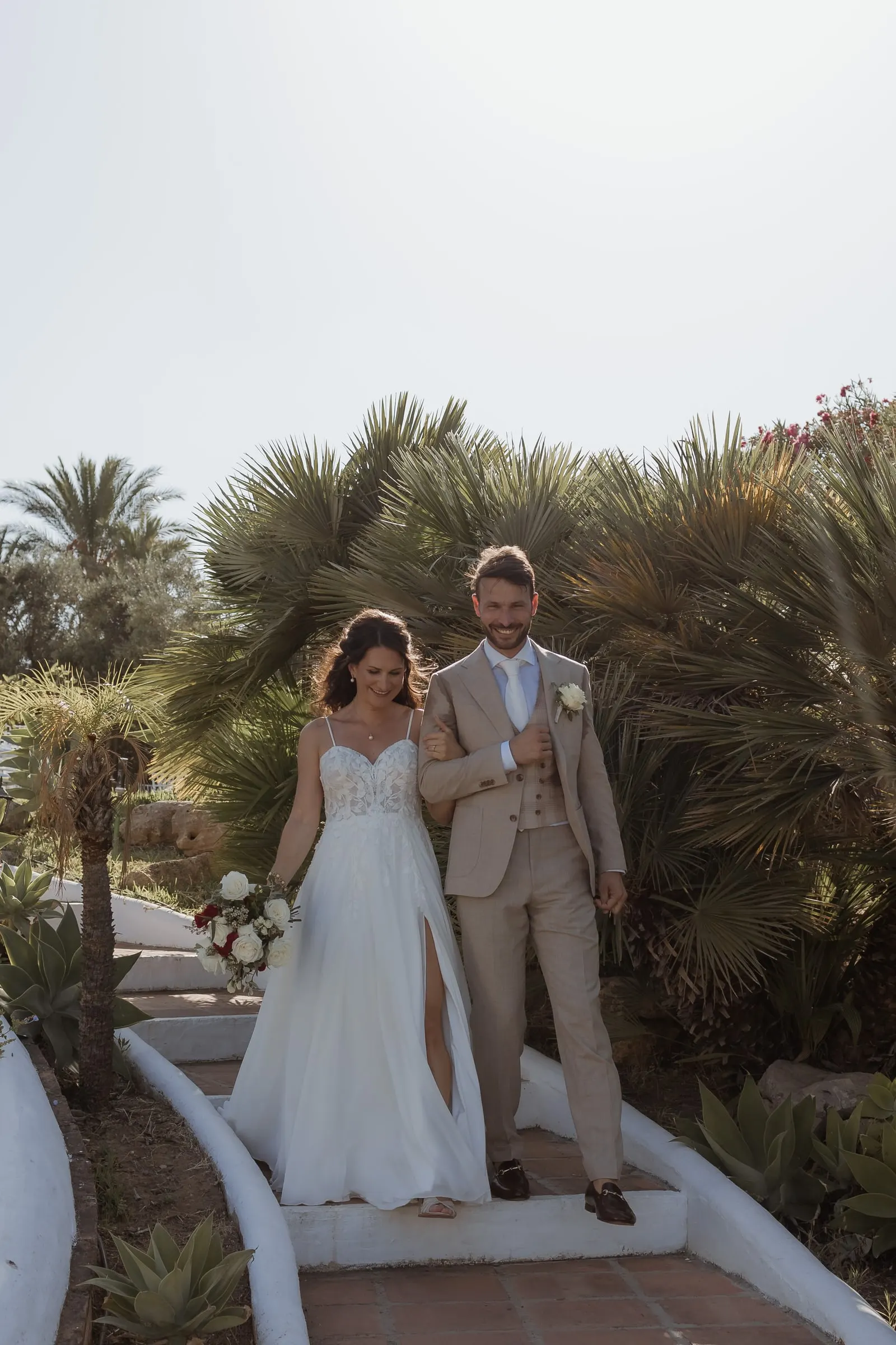 Los novios bajan de la mano unos escalones encalados entre palmeras, Hacienda San José, Mijas