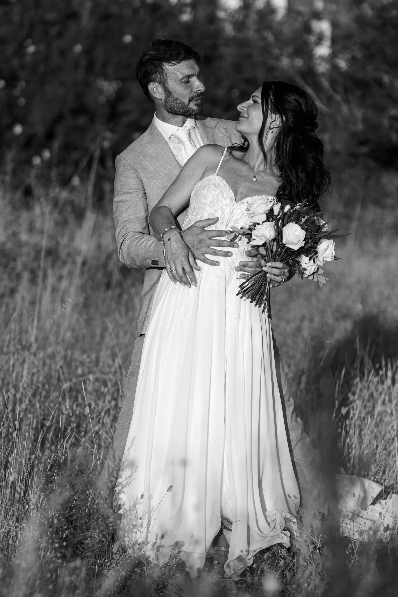 El novio abraza a la novia por detrás entre la hierba alta, en blanco y negro, Hacienda San José, Mijas