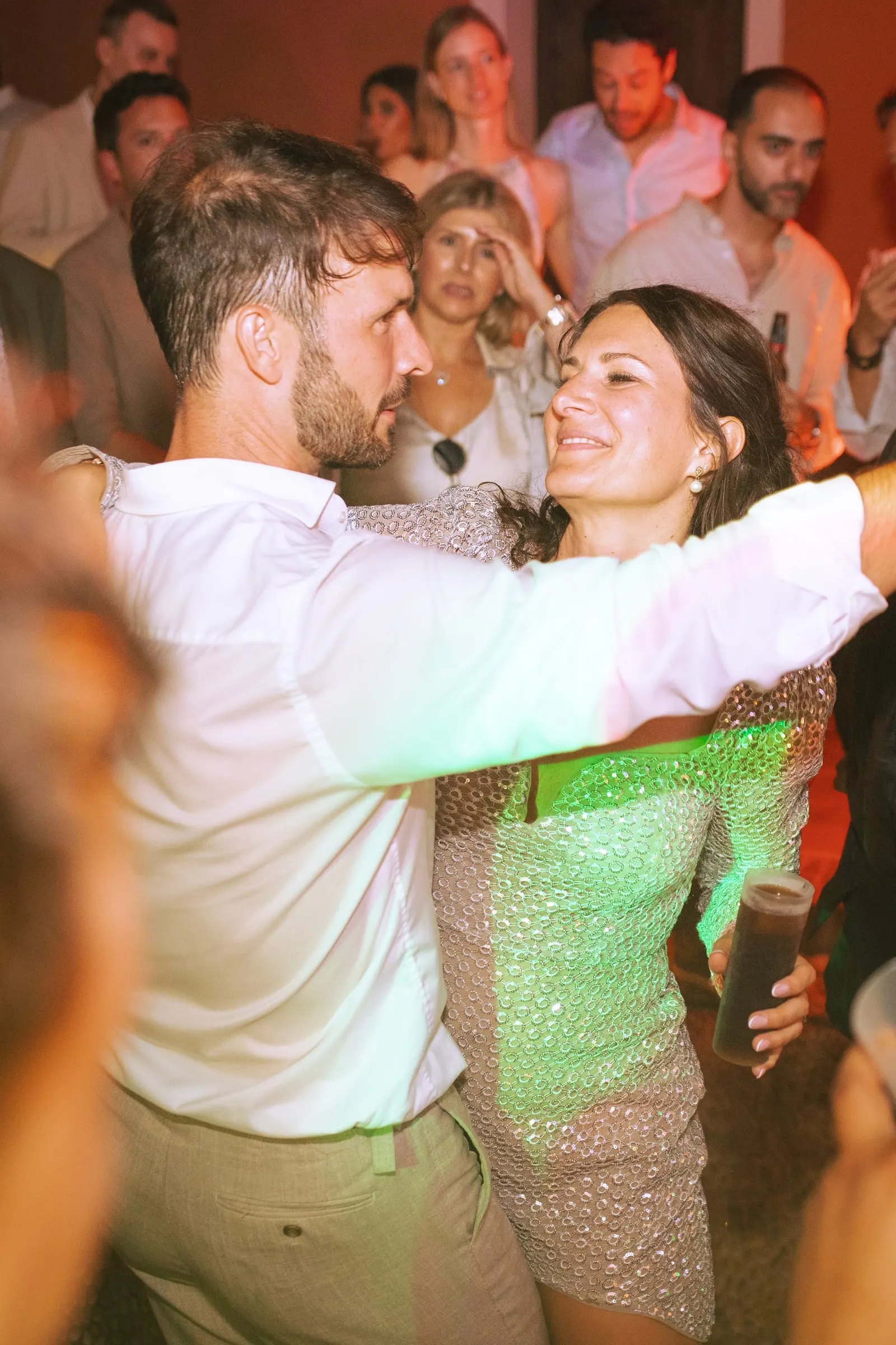 El novio y una invitada con vestido de lentejuelas bailan entre la gente por la noche, Hacienda San José, Mijas