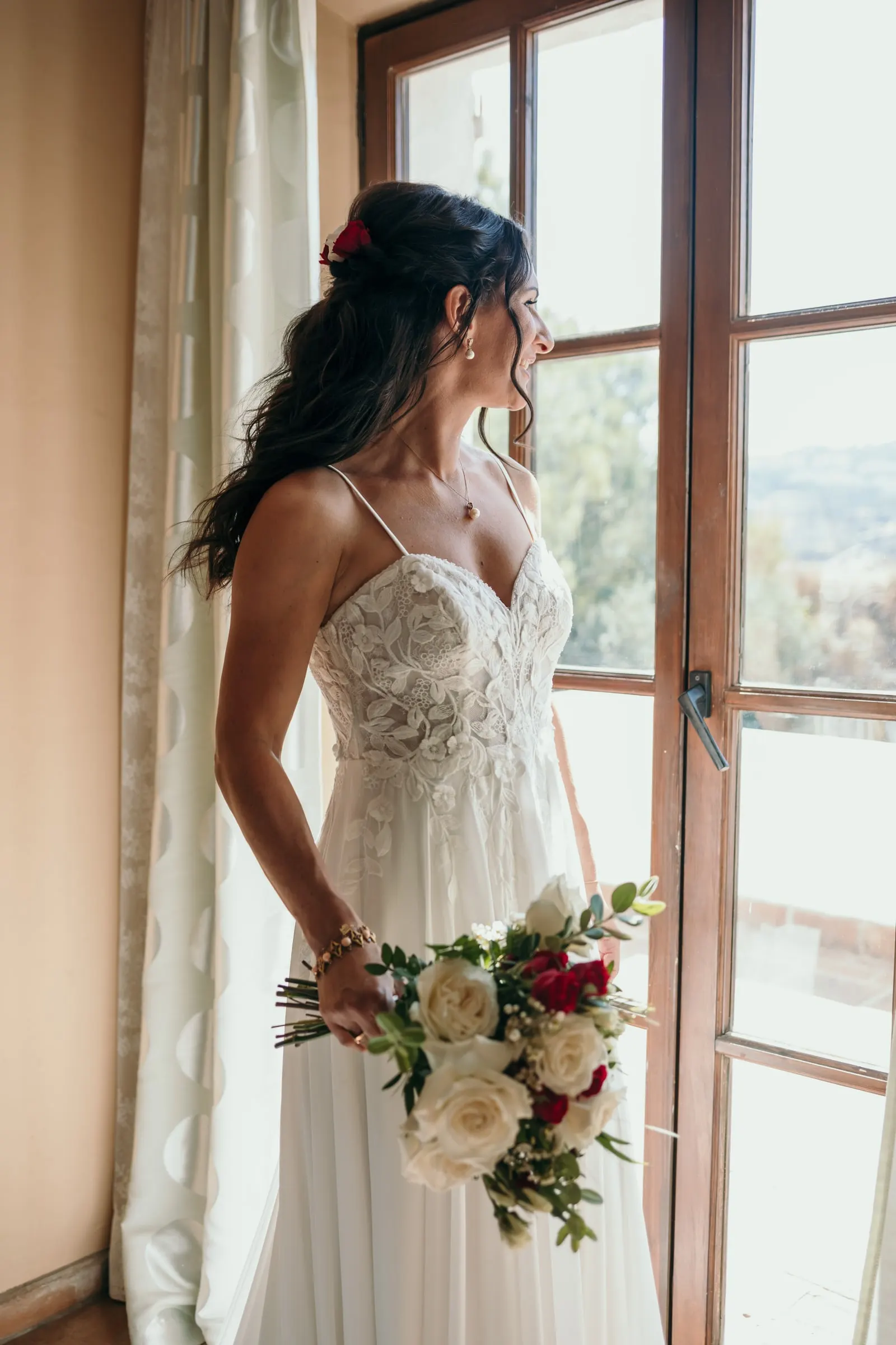 La novia mira por un ventanal con su ramo de rosas en la mano, Hacienda San José, Mijas