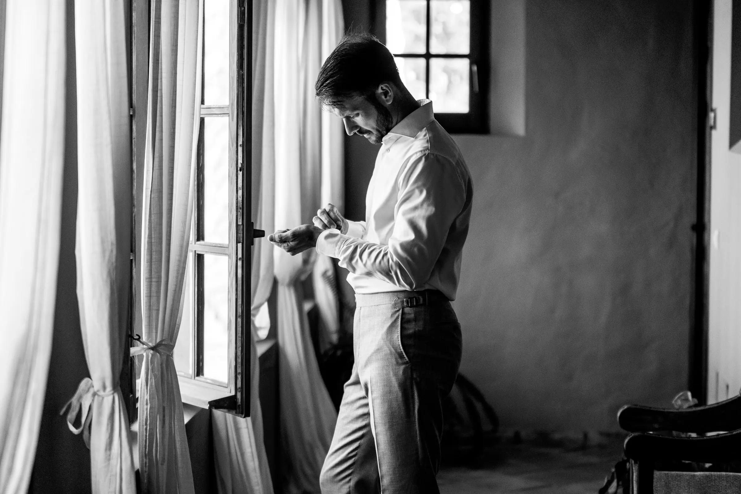El novio se ajusta los gemelos junto a un ventanal, en blanco y negro, Hacienda San José, Mijas