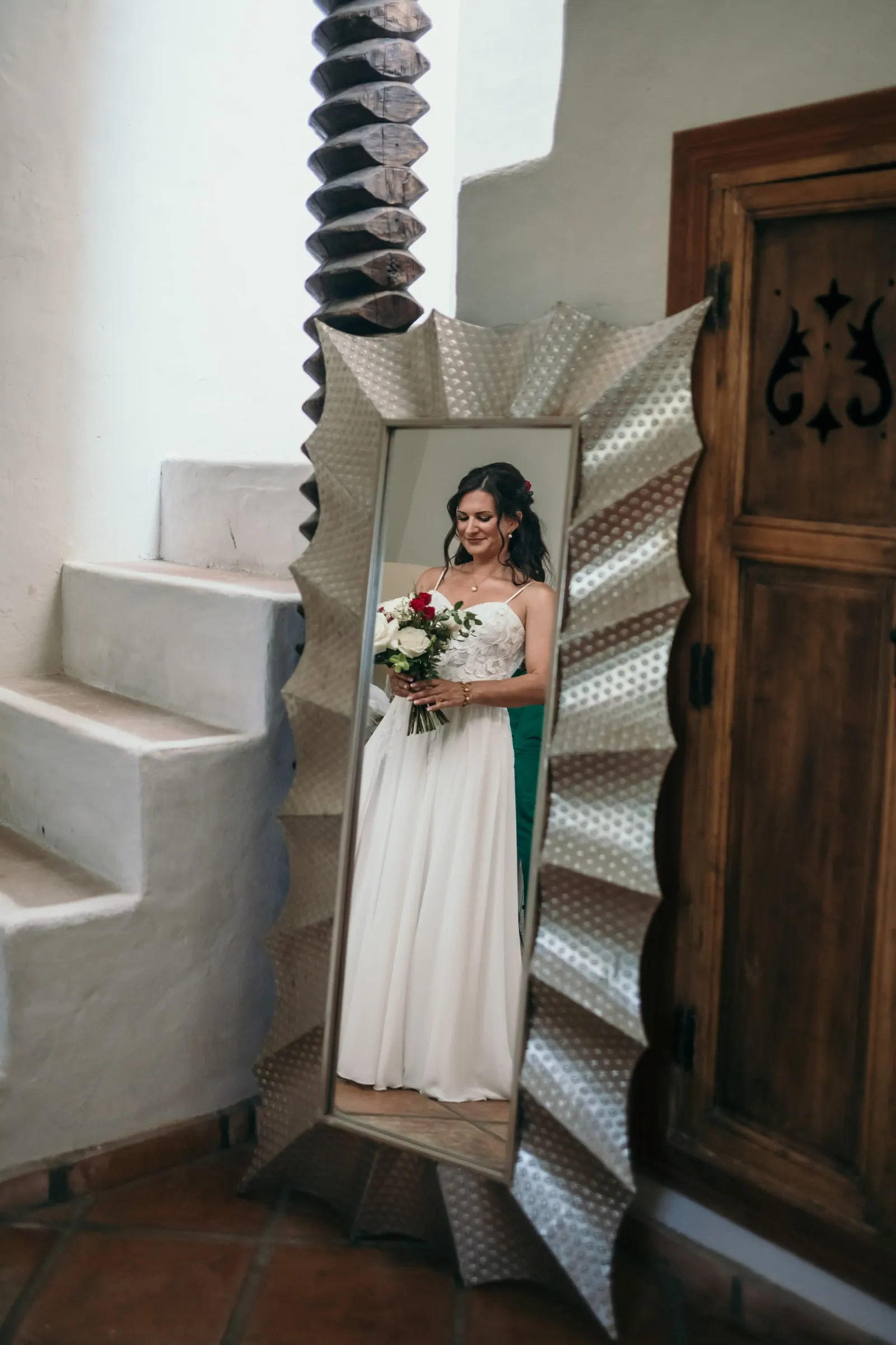 La novia reflejada en un gran espejo plateado junto a una puerta de madera tallada, Hacienda San José, Mijas