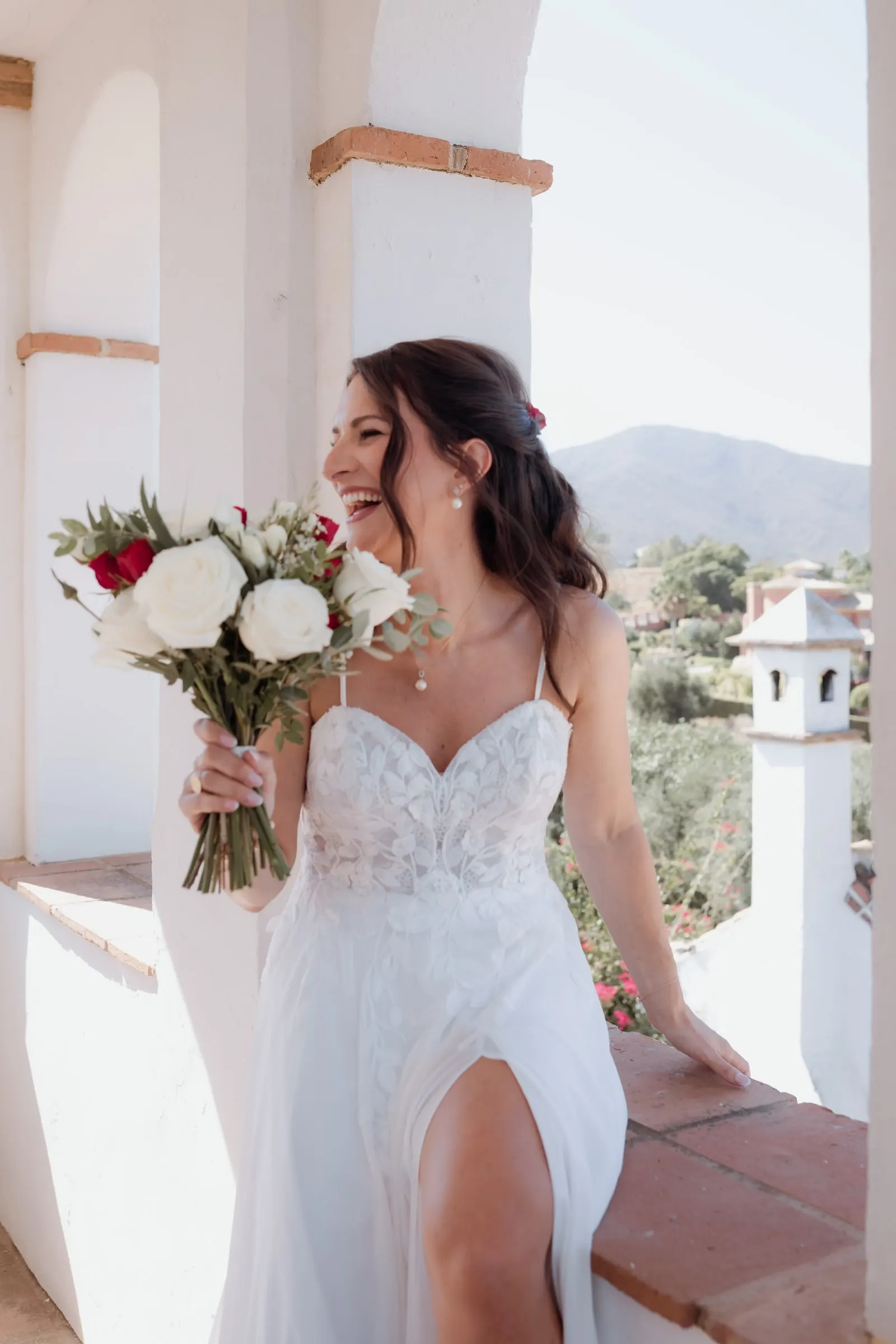 La novia se ríe en un balcón encalado y soleado con las colinas detrás, Hacienda San José, Mijas
