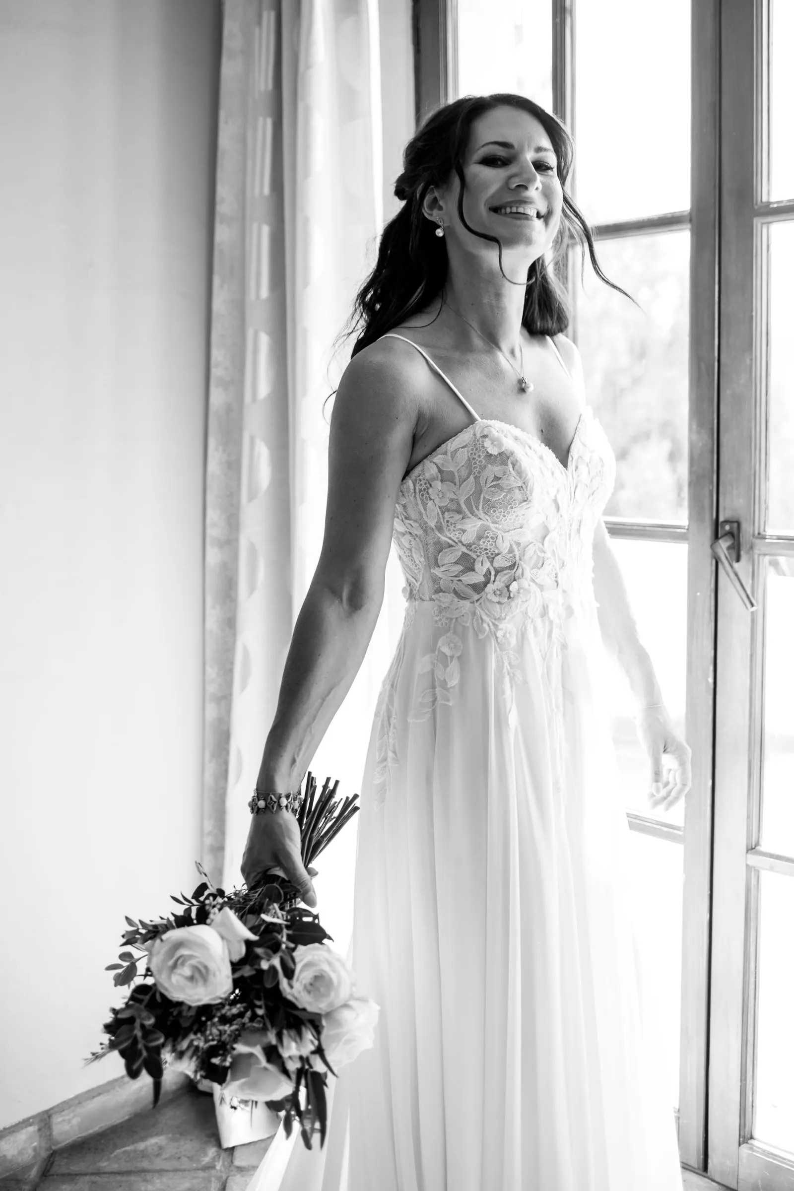 La novia sonríe junto a una ventana abierta con el ramo en la mano, en blanco y negro, Hacienda San José, Mijas
