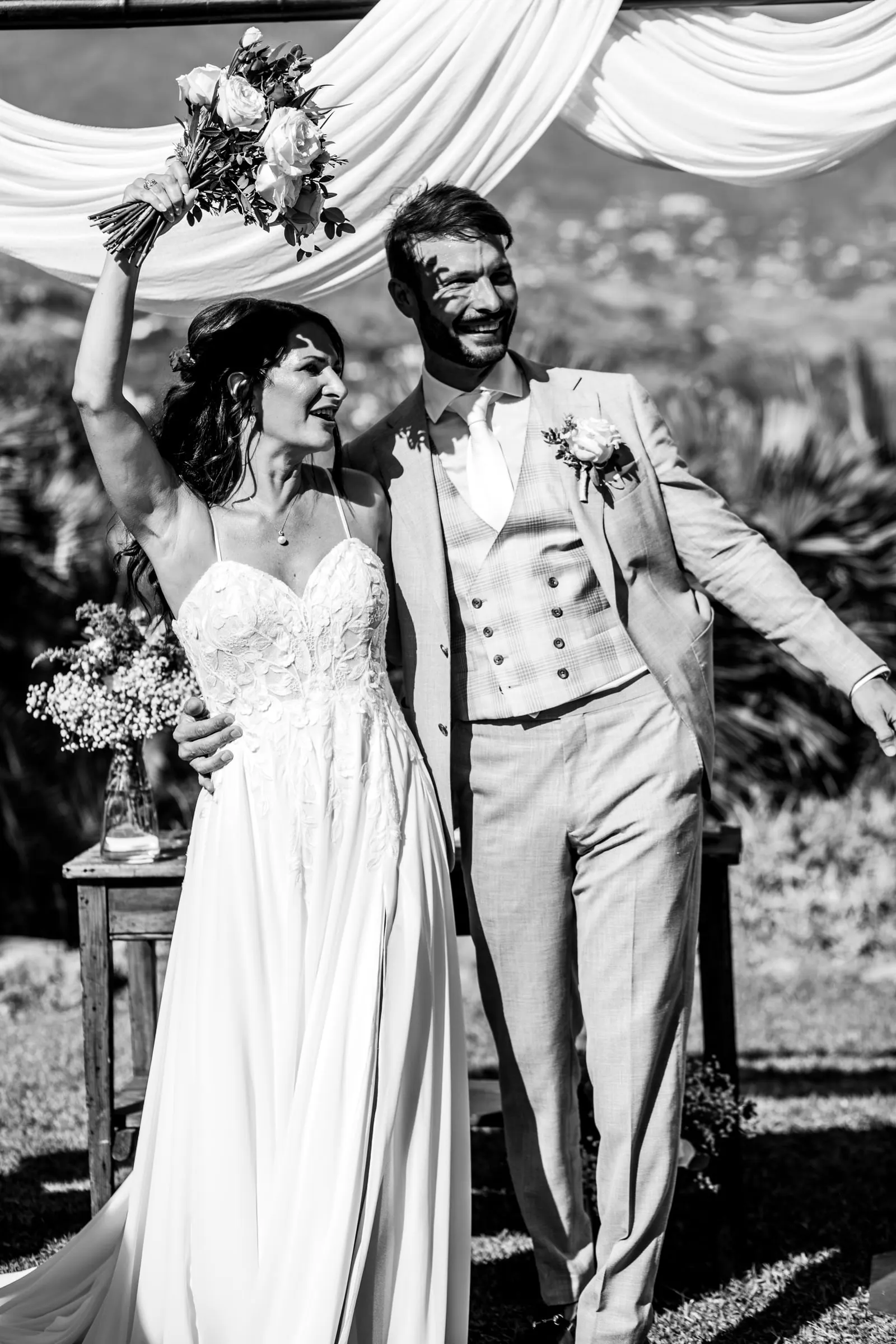 Los recién casados celebran junto al dosel con el ramo en alto, en blanco y negro, Hacienda San José, Mijas