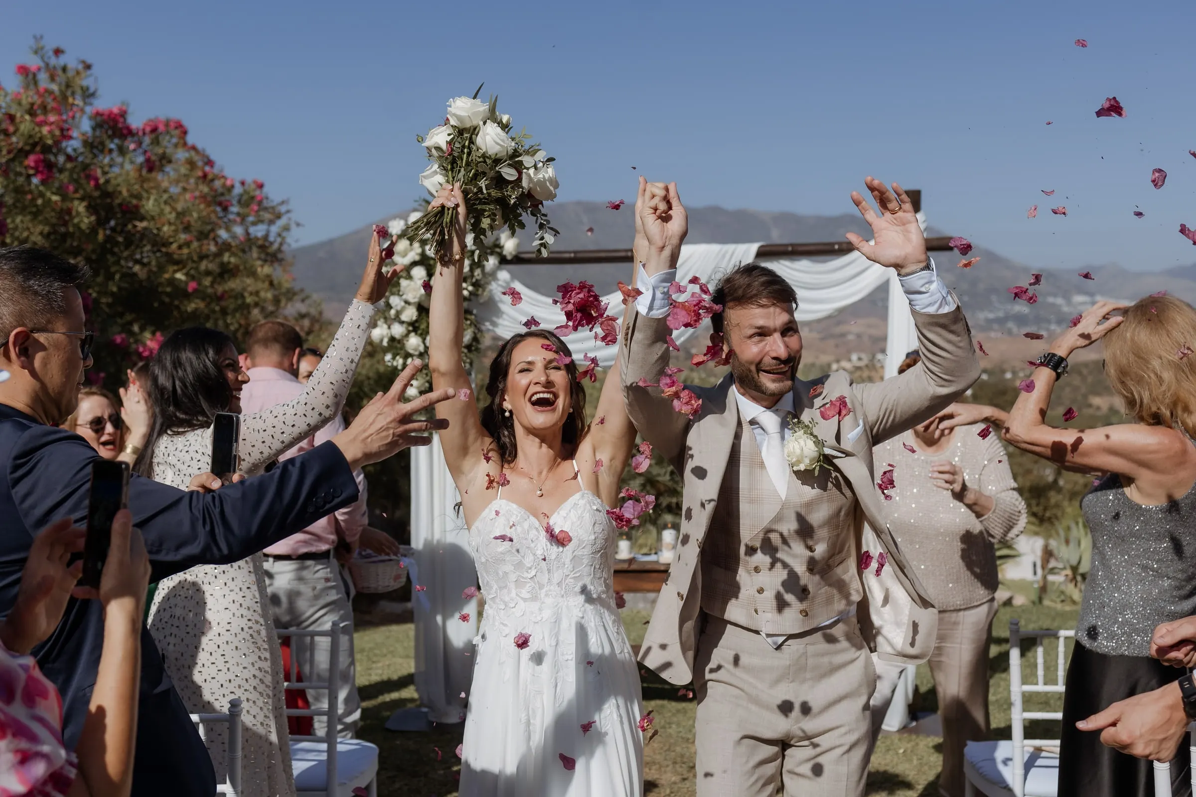 Los novios ríen bajo una nube de pétalos rojos mientras los invitados les rodean, Hacienda San José, Mijas