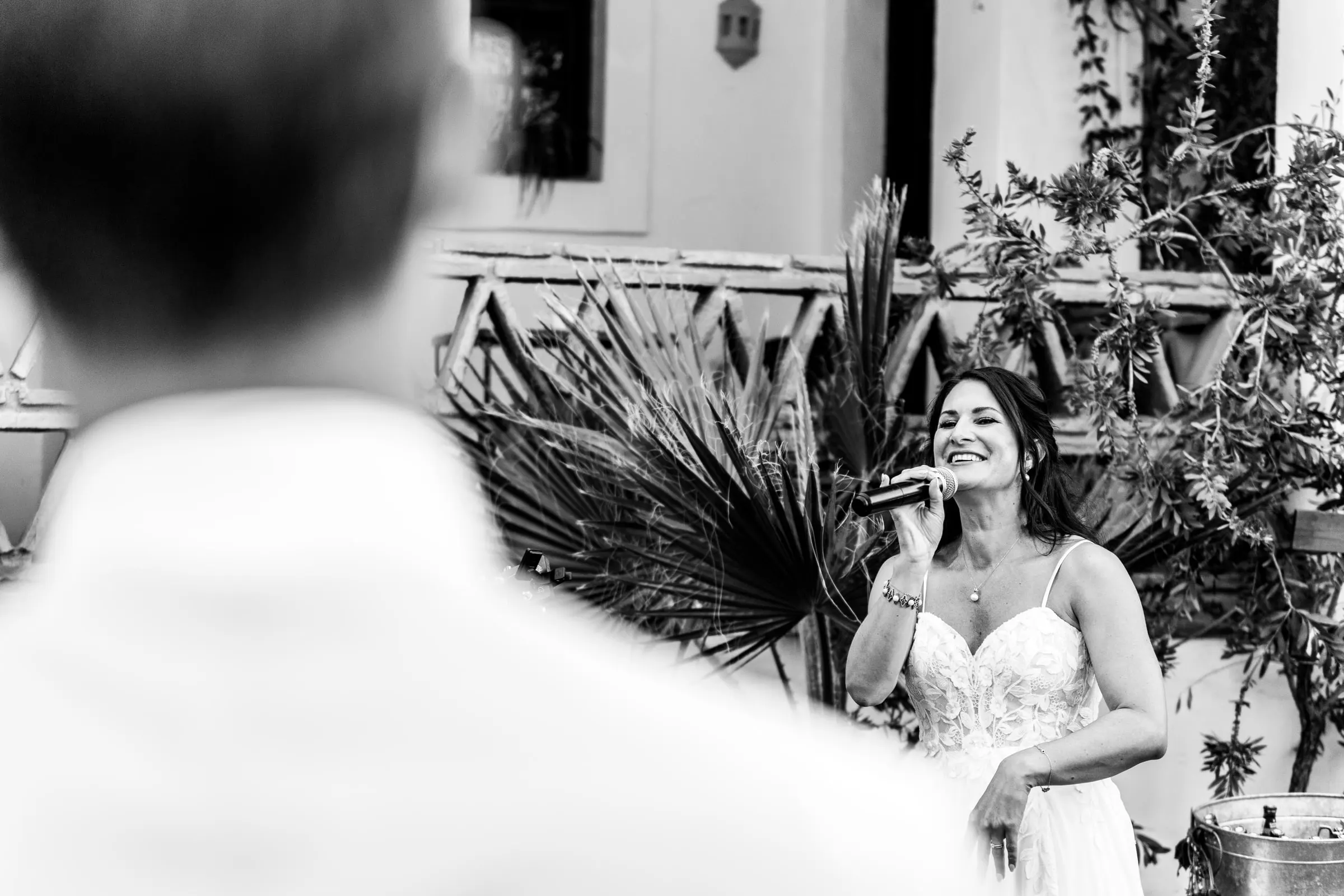 La novia canta al micrófono delante de unas hojas de palmera, en blanco y negro, Hacienda San José, Mijas
