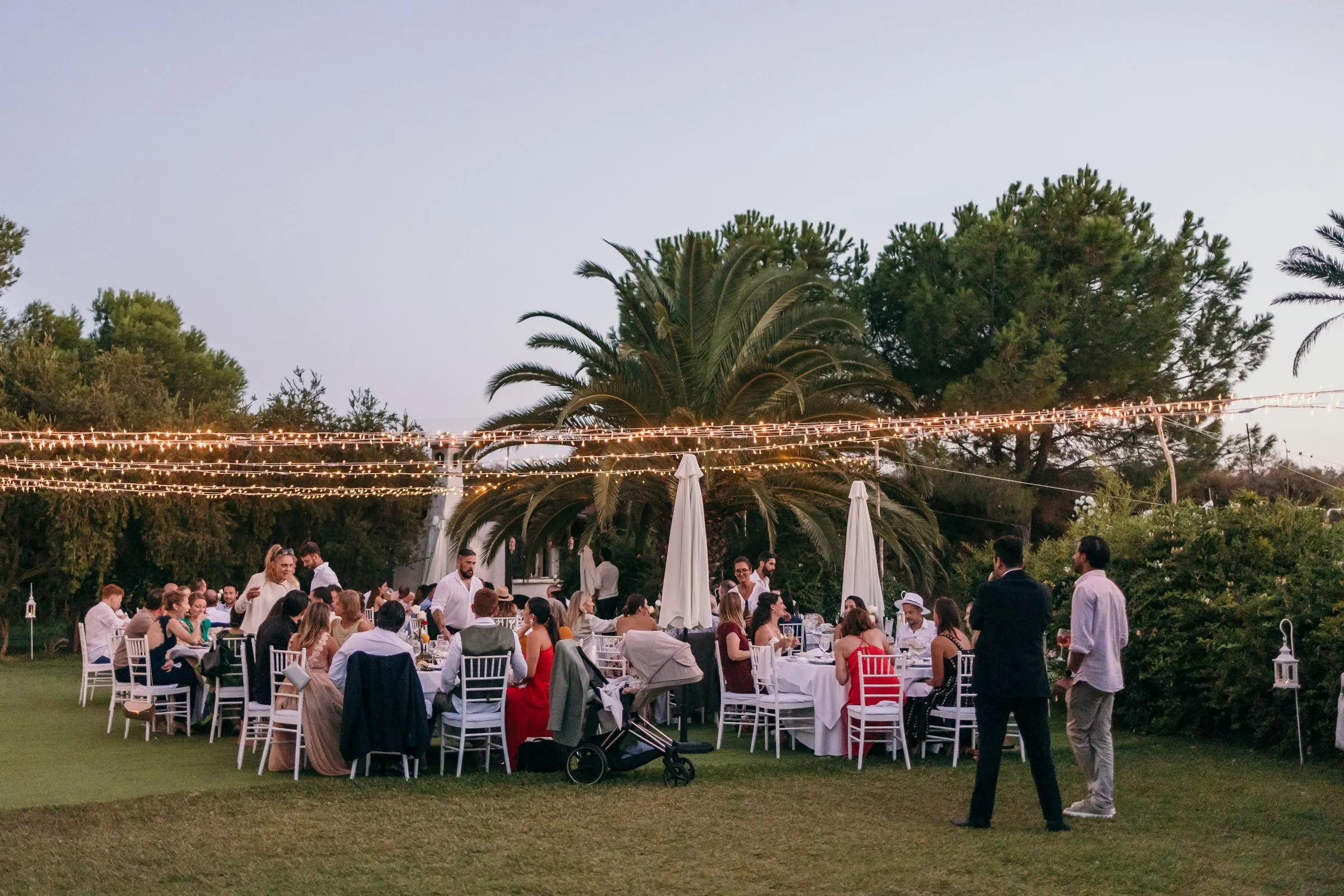 Los invitados cenan en el césped bajo guirnaldas de luces y palmeras al anochecer, Hacienda San José, Mijas