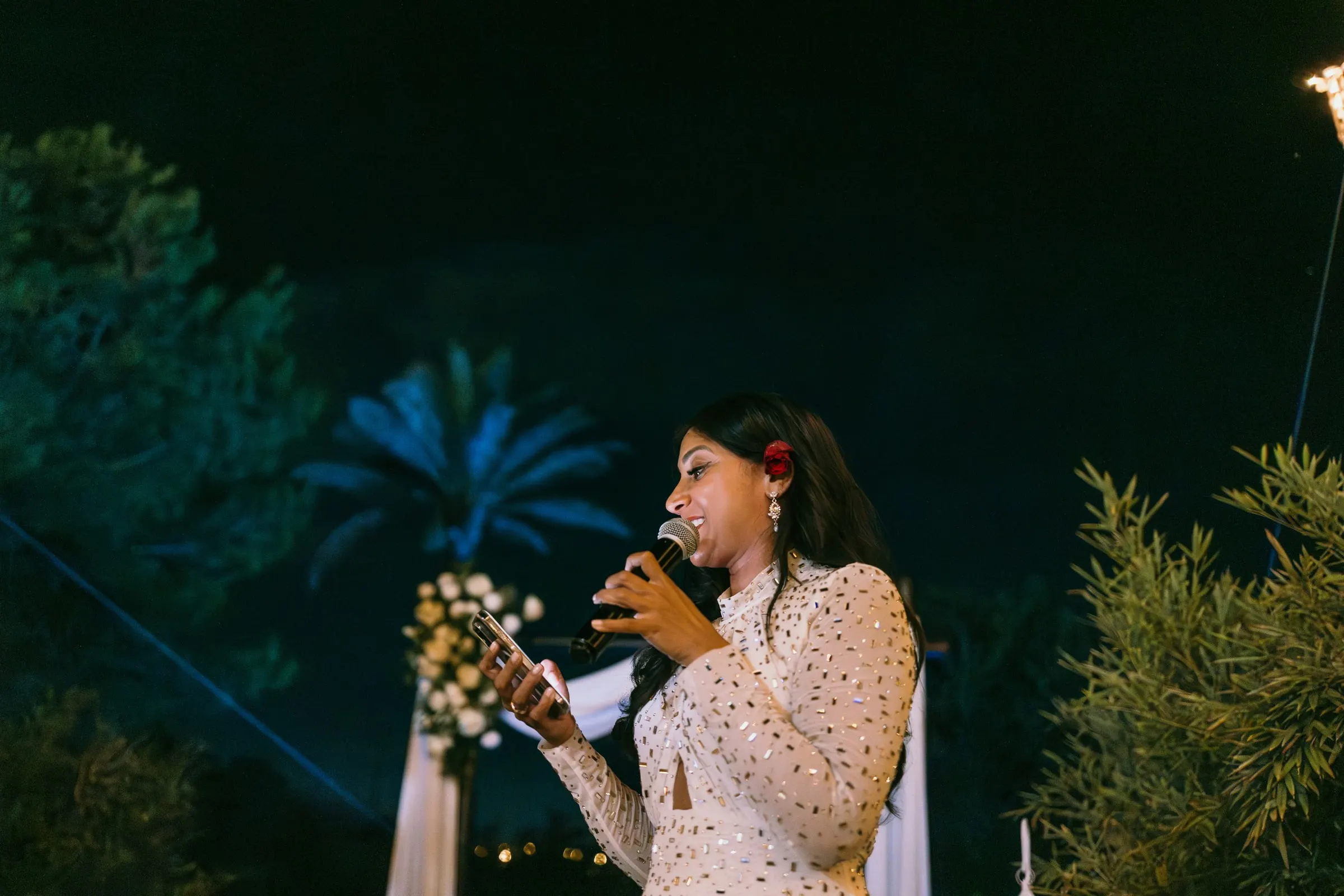 Una invitada con vestido blanco de lunares lee un discurso al micrófono de noche, Hacienda San José, Mijas