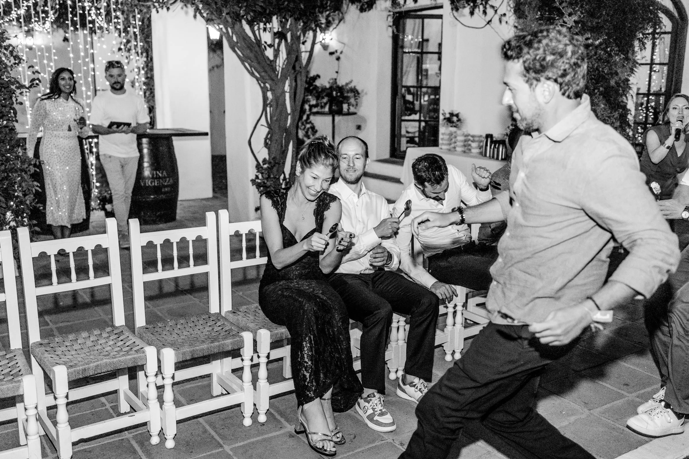 Un invitado pasa bailando delante de amigos sentados en sillas blancas, en blanco y negro, Hacienda San José, Mijas