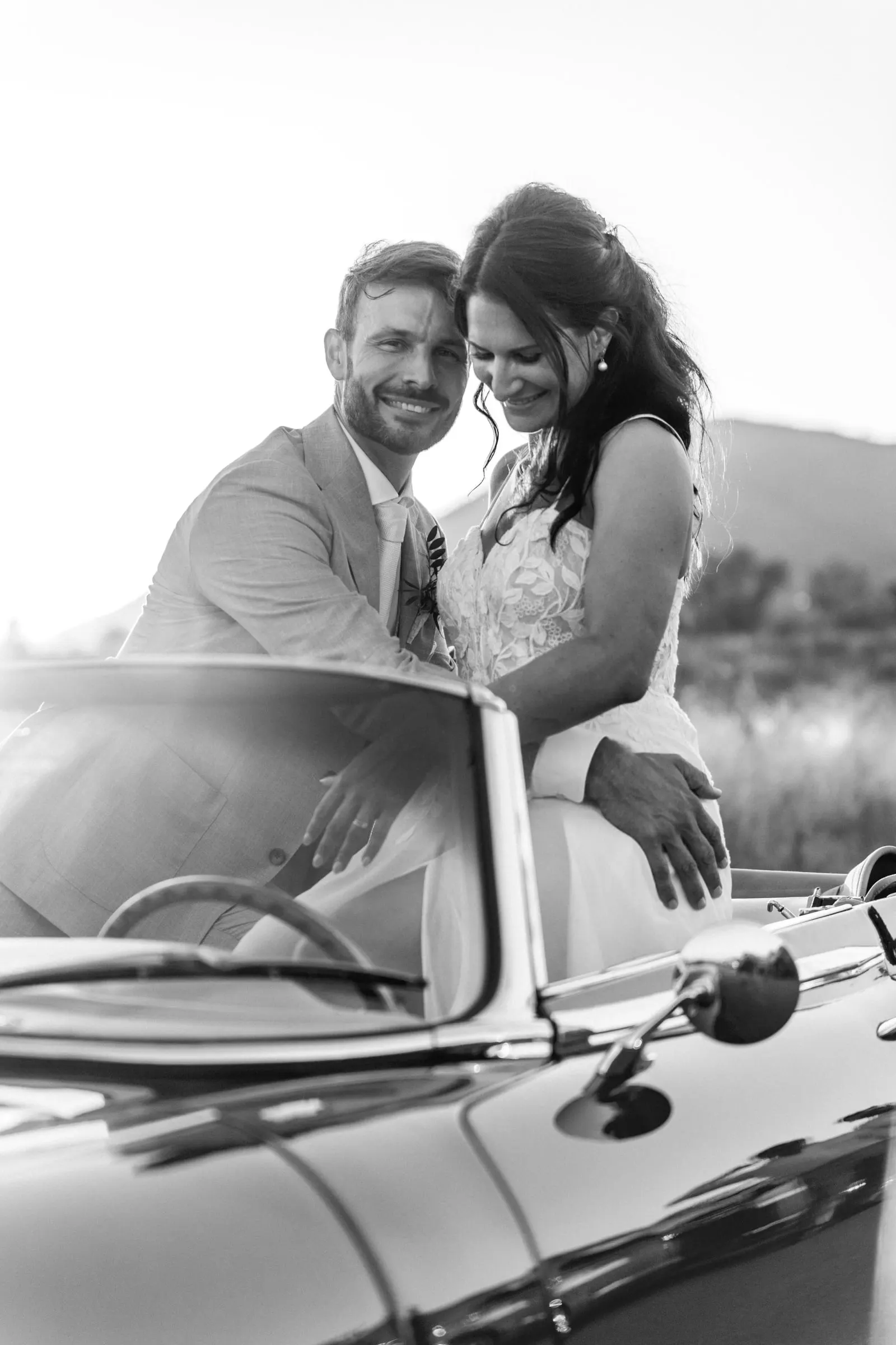 Los novios sonríen juntos en un descapotable, con el novio al volante, en blanco y negro, Hacienda San José, Mijas