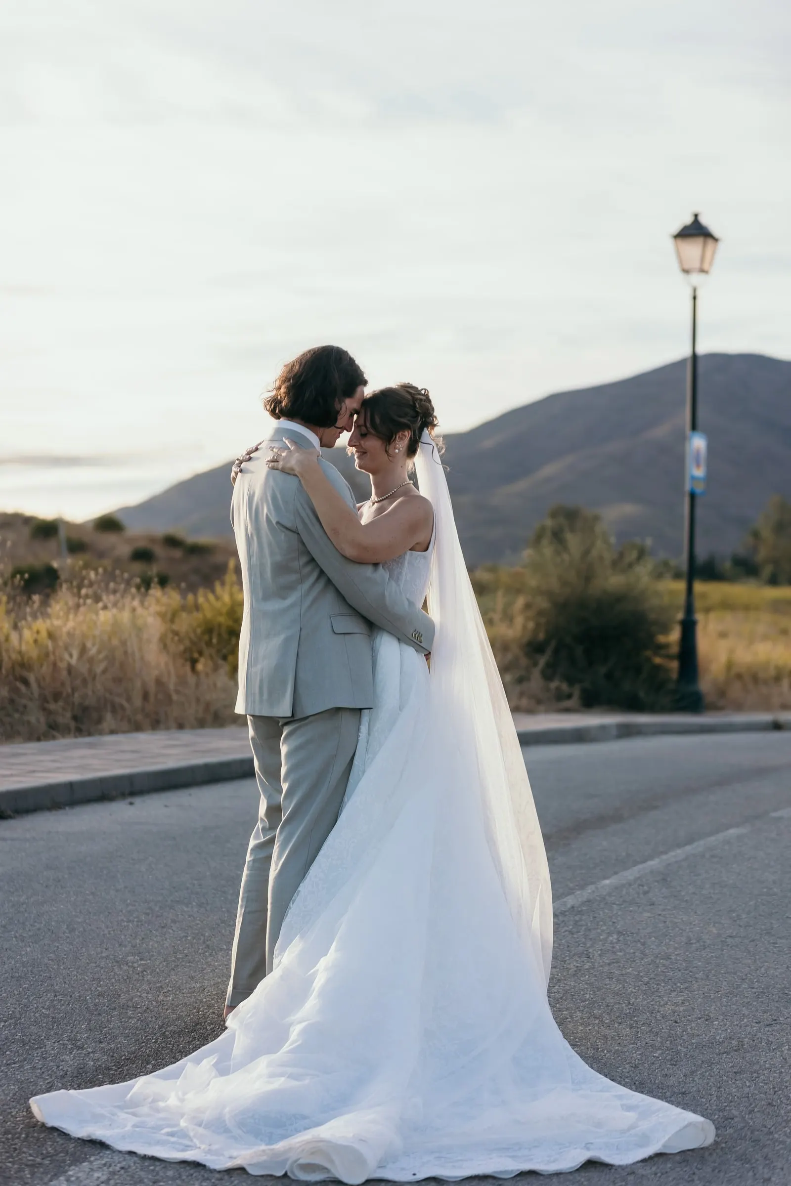 The couple embracing on a quiet road, her long veil and train trailing, Hacienda San José, Mijas