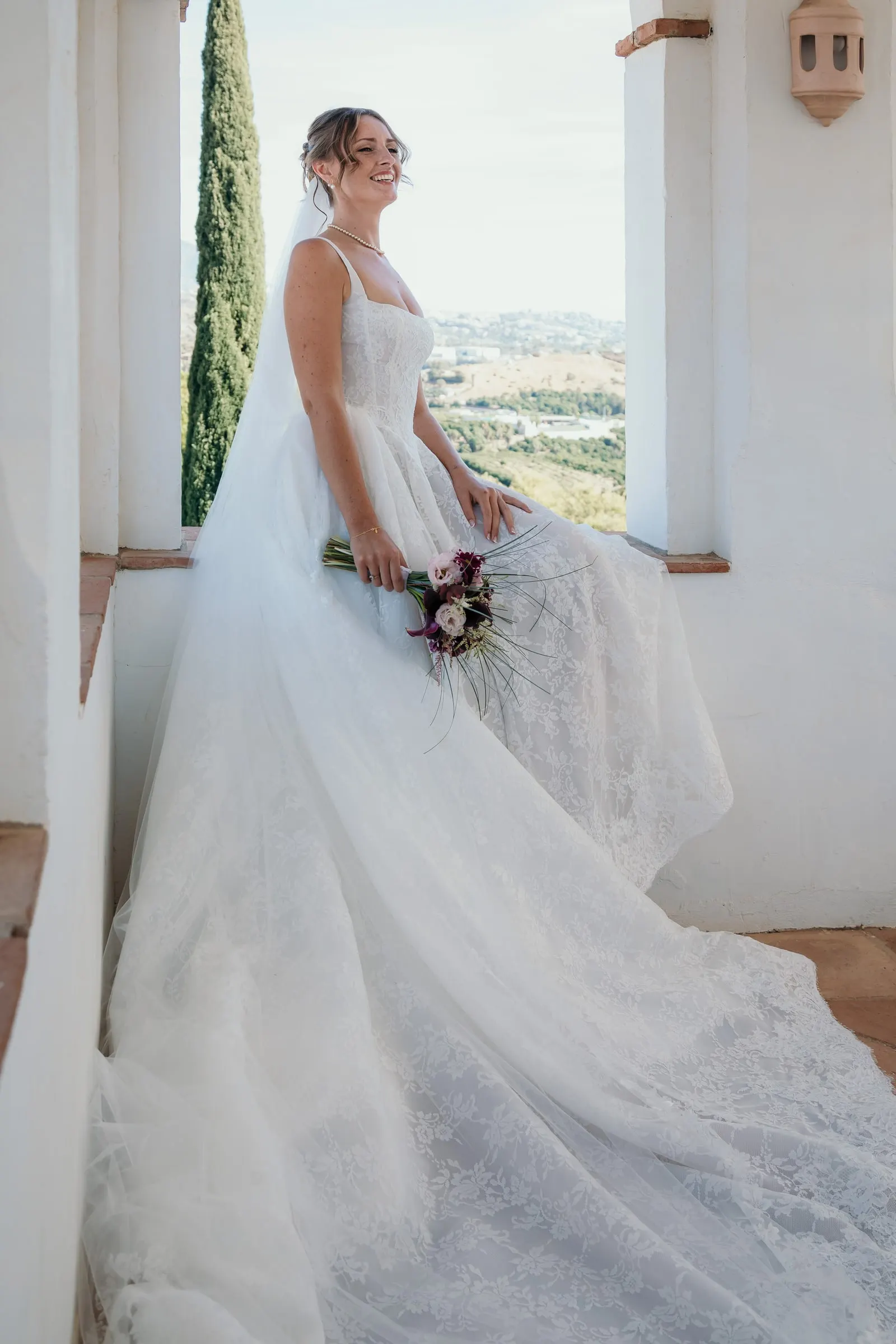 The bride sitting on a whitewashed window ledge, her train spilling to the floor, Hacienda San José, Mijas