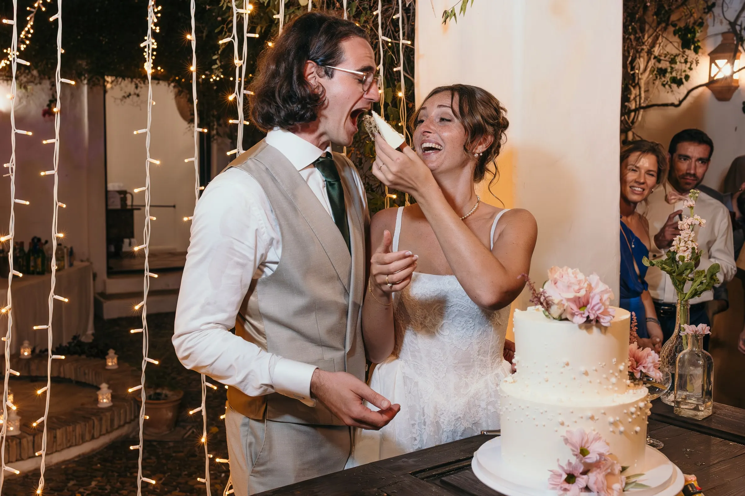 Bride feeding the groom a piece of wedding cake as both laugh at Hacienda San José, Mijas