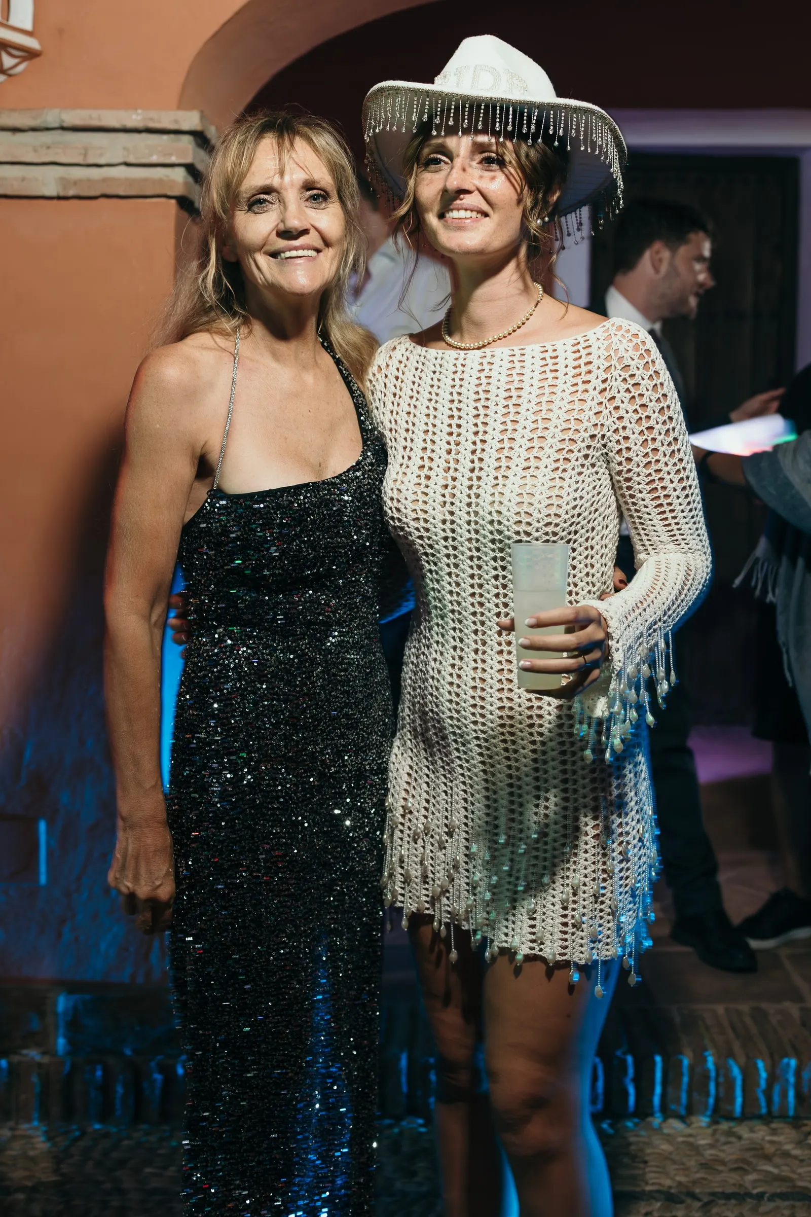 Bride in a crochet dress and a white cowboy hat posing with a guest at the party at Hacienda San José, Mijas