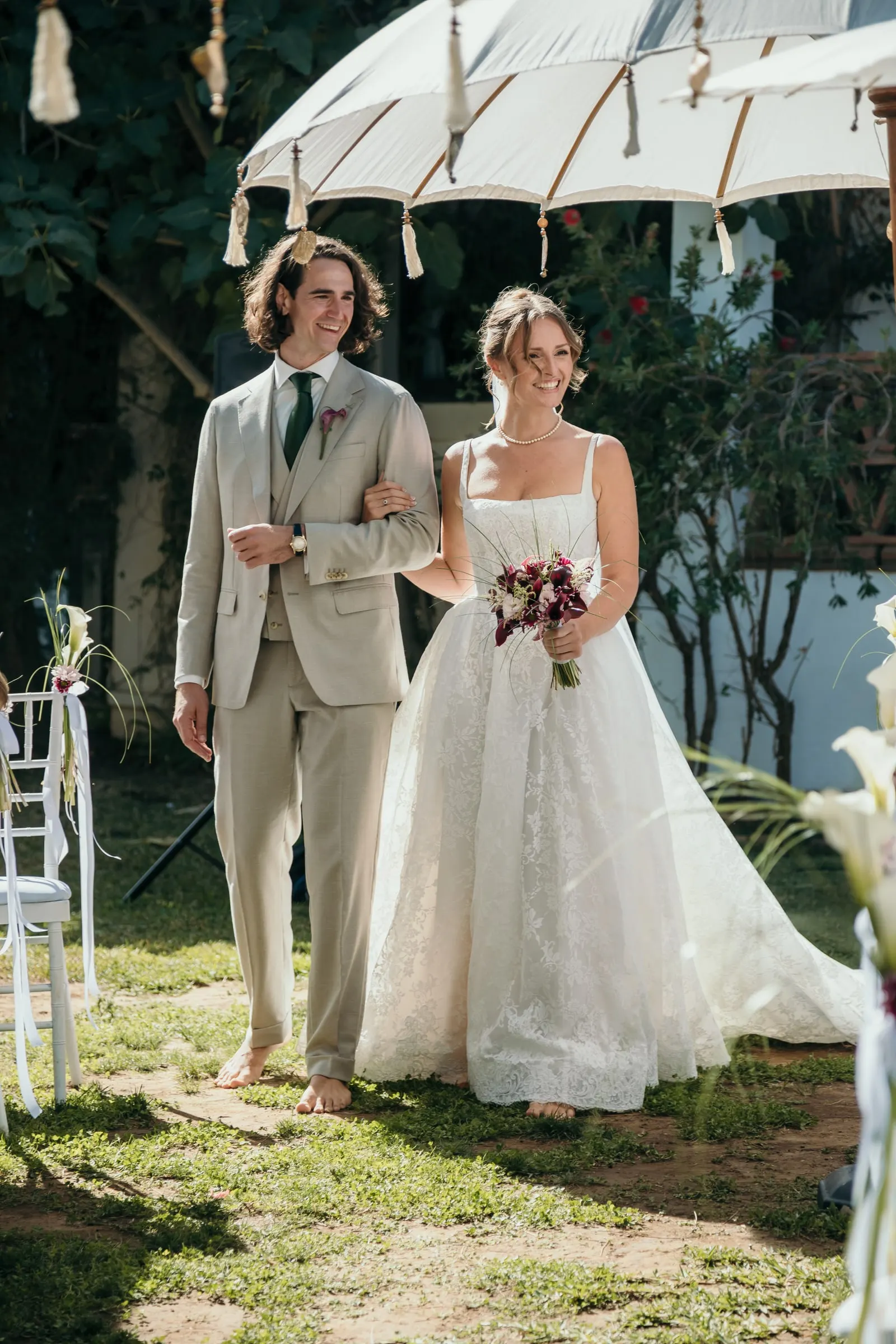 The barefoot couple walking arm in arm towards the ceremony under a parasol, Hacienda San José, Mijas