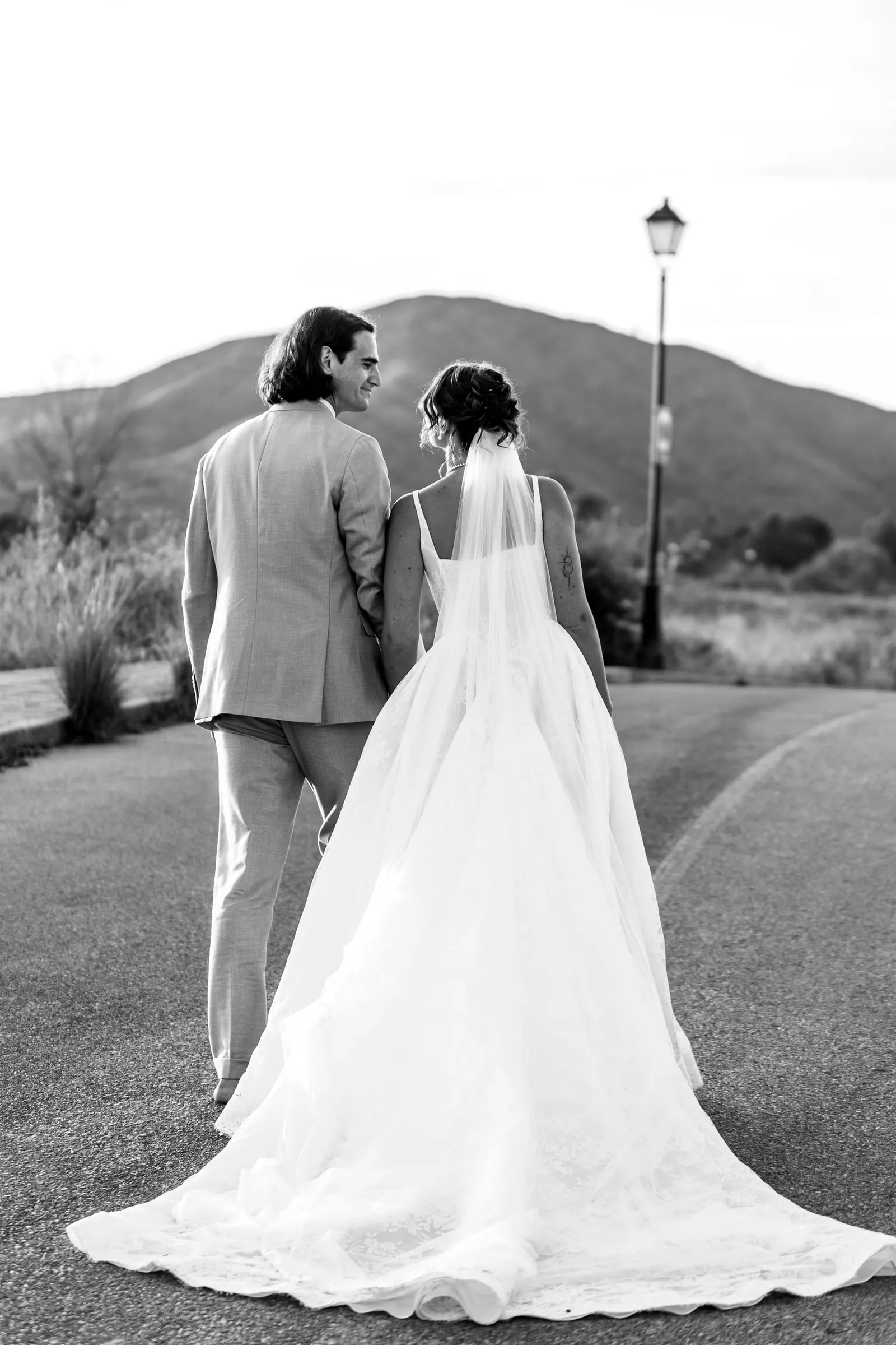 Black and white of the couple walking away down a road, her long train behind, Hacienda San José, Mijas