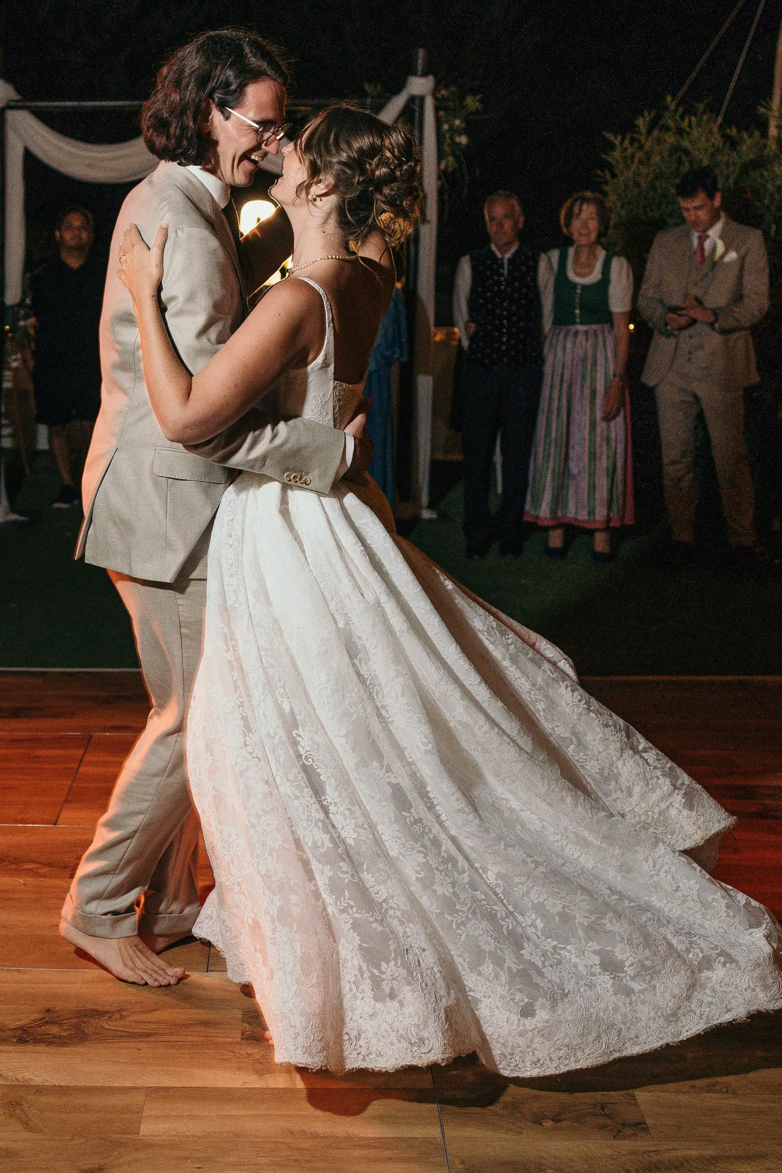 Bride and groom dancing close at night as family watches from the edge of the floor, Hacienda San José, Mijas