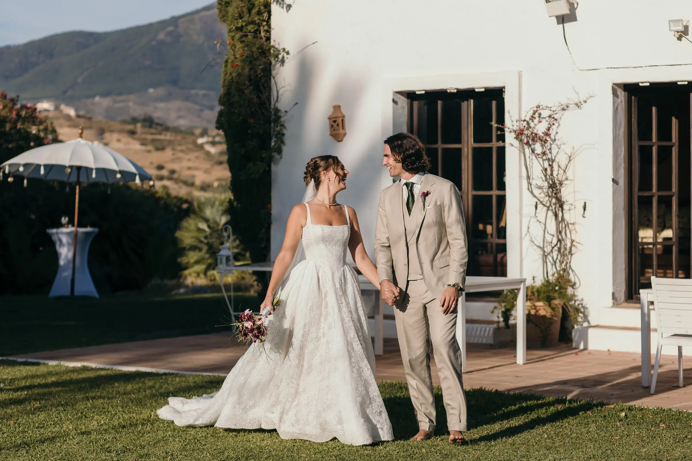 Bride and groom walking hand in hand past the white house and a parasol, Hacienda San José, Mijas