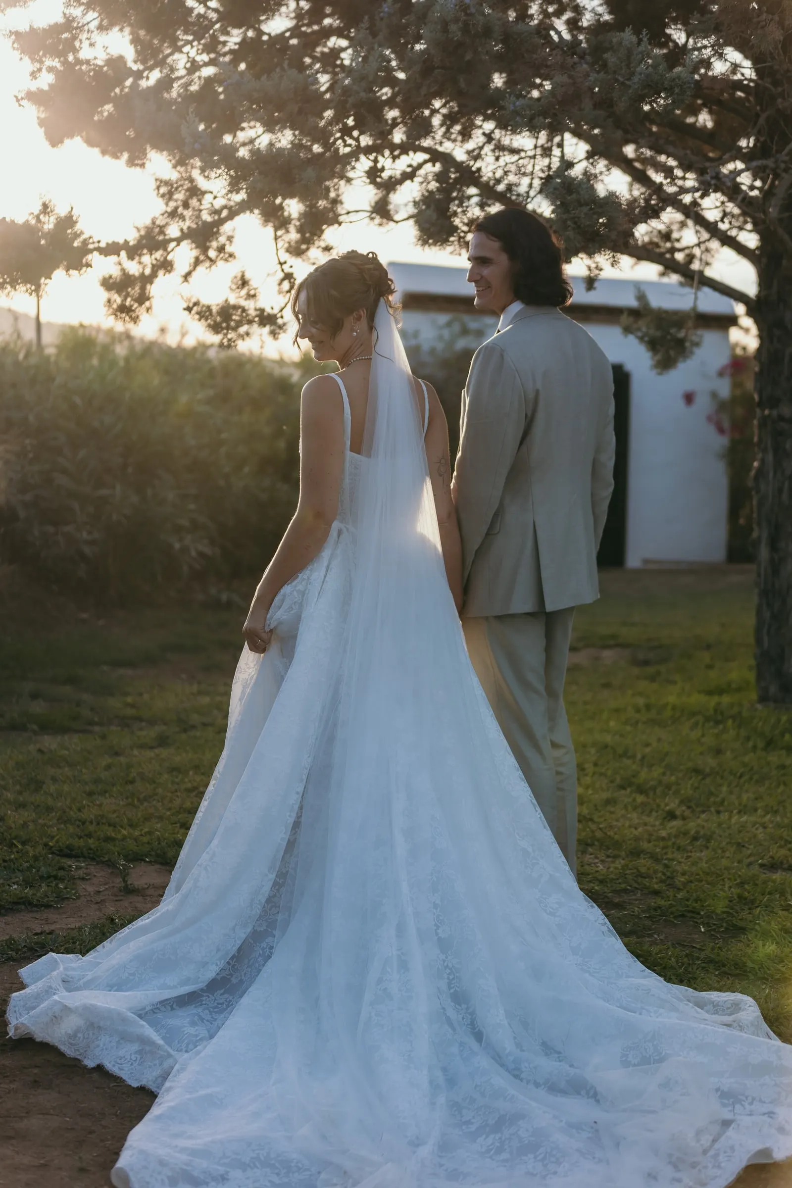 The couple seen from behind on the lawn at sunset, her long veil and train spread out, Hacienda San José, Mijas