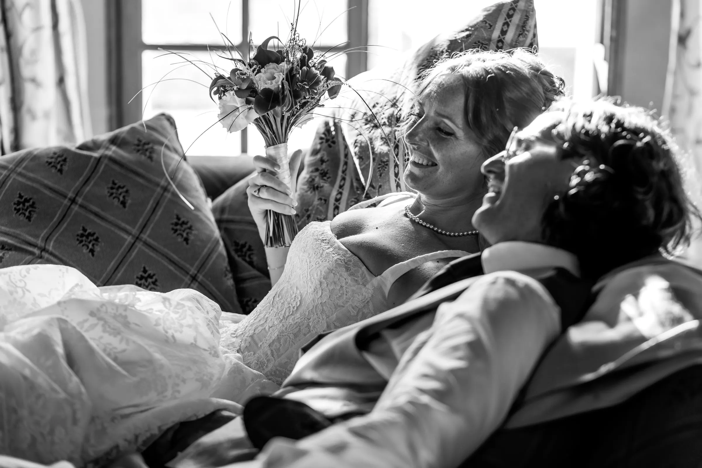 Black and white of the couple laughing as they lie back together on a sofa, Hacienda San José, Mijas
