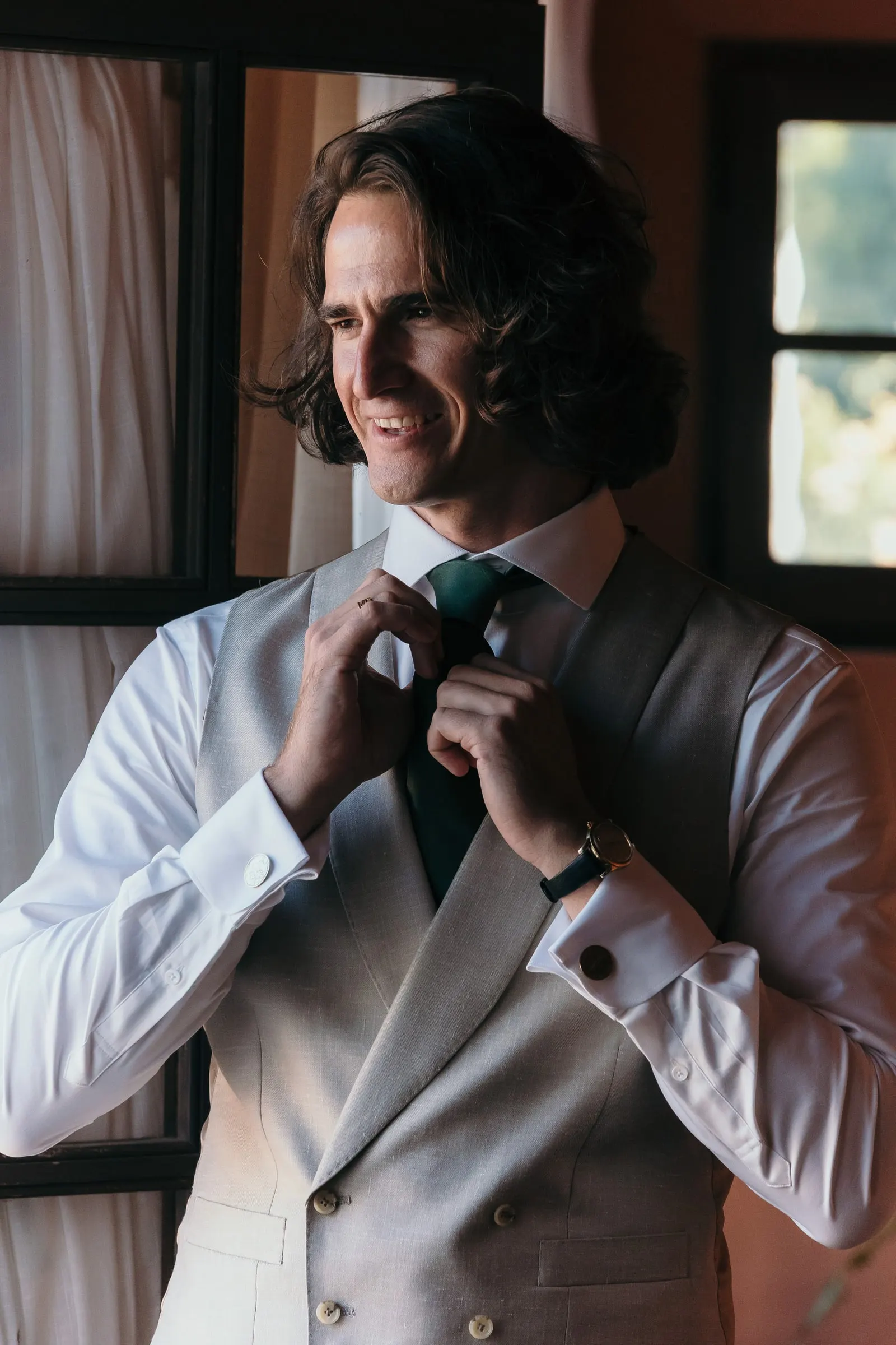 The groom smiling as he straightens his green tie by the window, Hacienda San José, Mijas