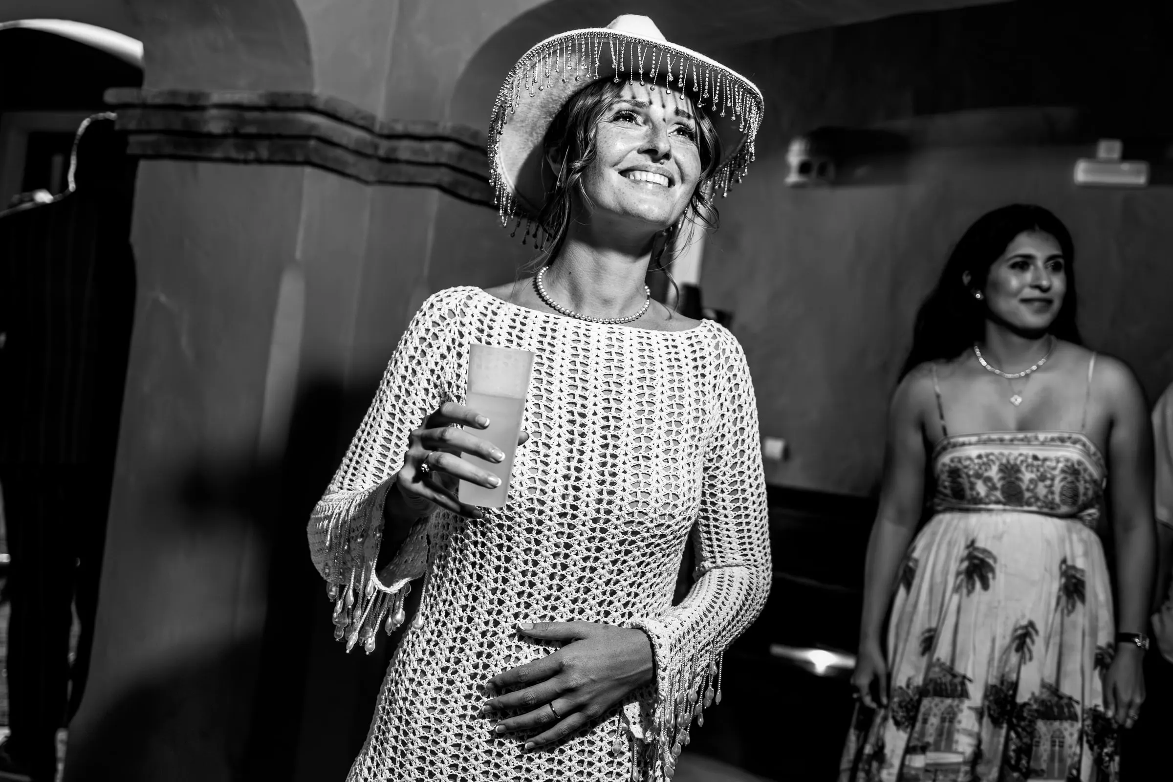 Black and white of the bride in a fringed hat and crochet dress laughing at the party, Hacienda San José, Mijas