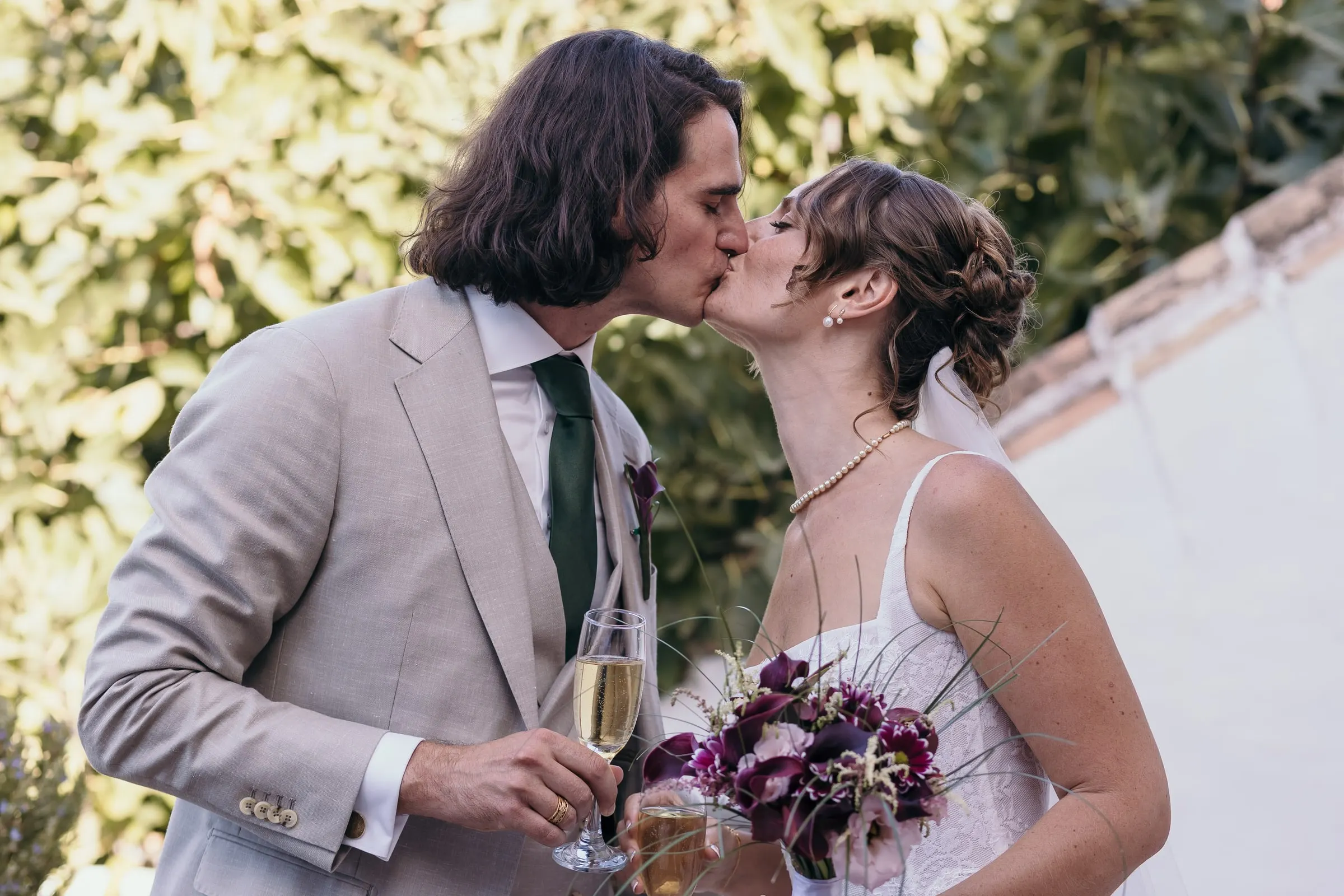 Bride and groom kissing with a glass of cava and her purple bouquet in hand, Hacienda San José, Mijas