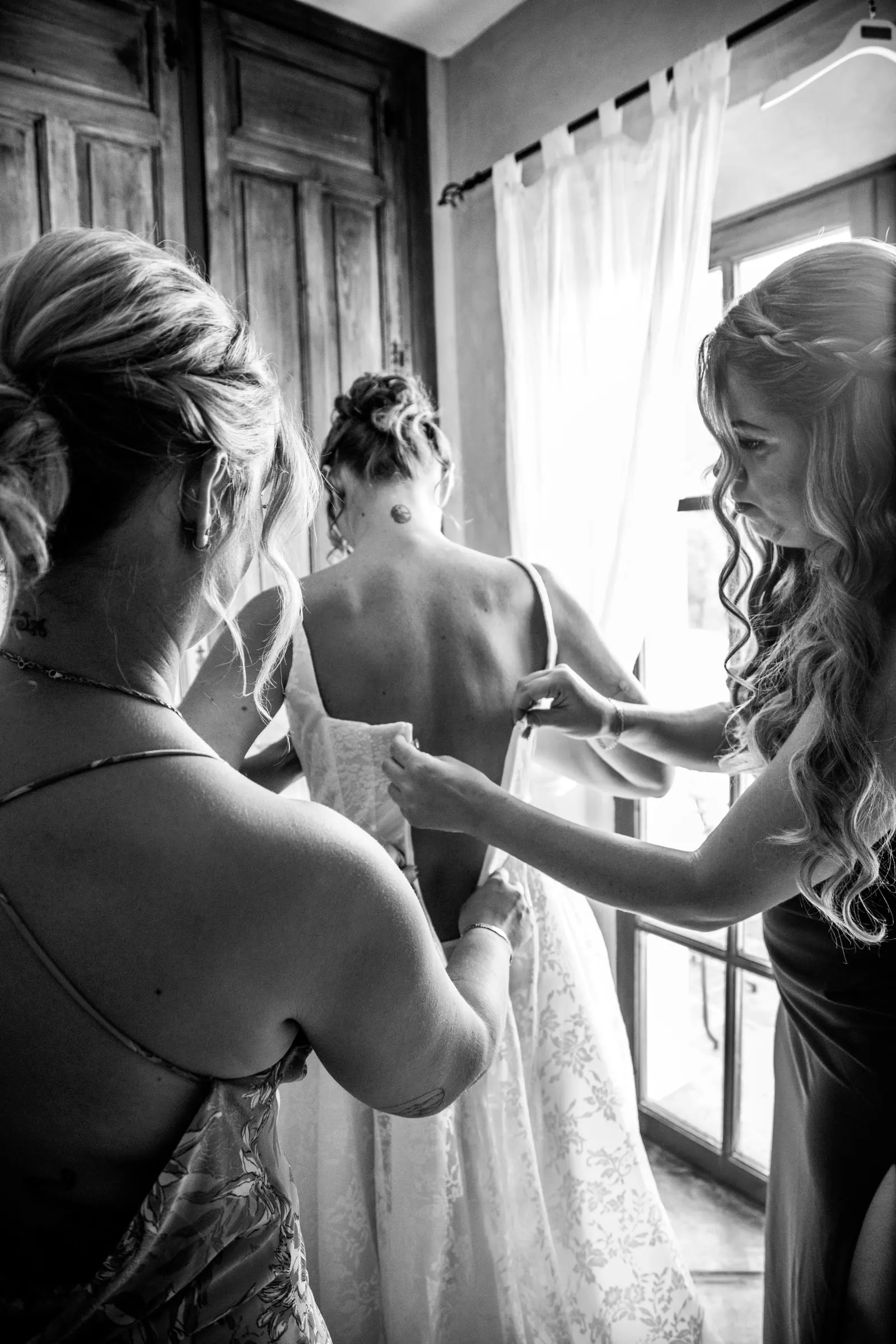 Black and white of two friends lacing up the bride's dress by the window, Hacienda San José, Mijas