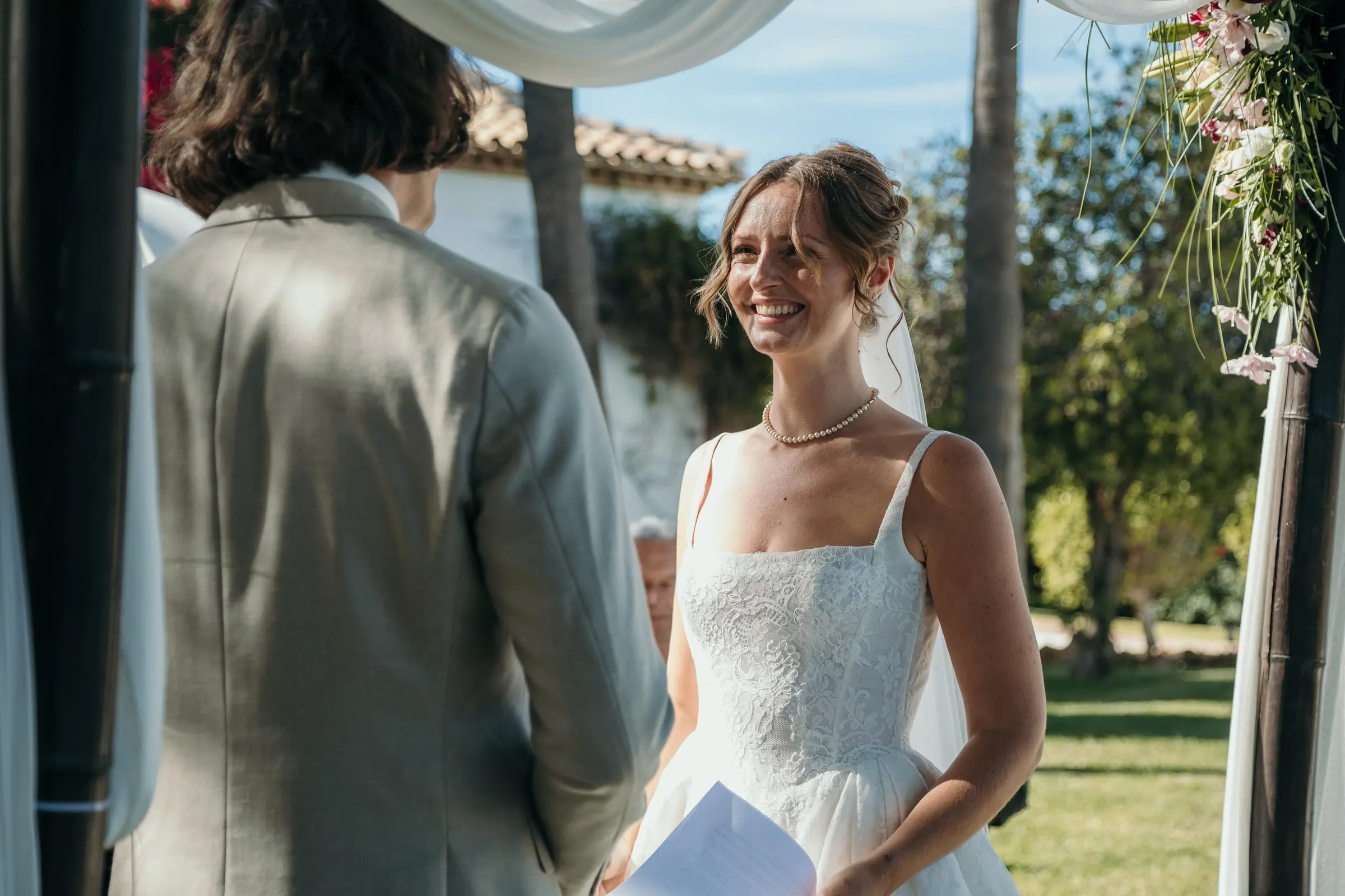 The bride smiling at the groom as she reads her vows under the canopy, Hacienda San José, Mijas