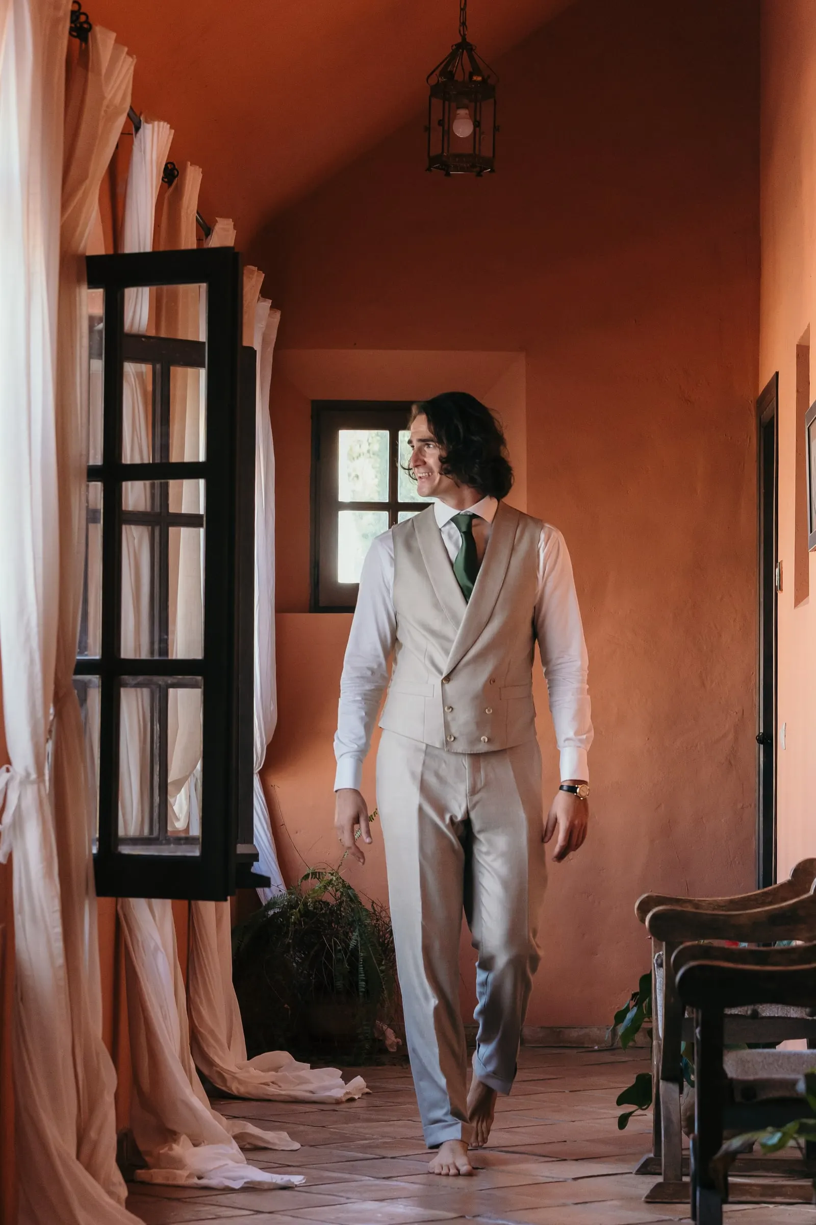 The groom in a waistcoat walking barefoot down a terracotta corridor, Hacienda San José, Mijas