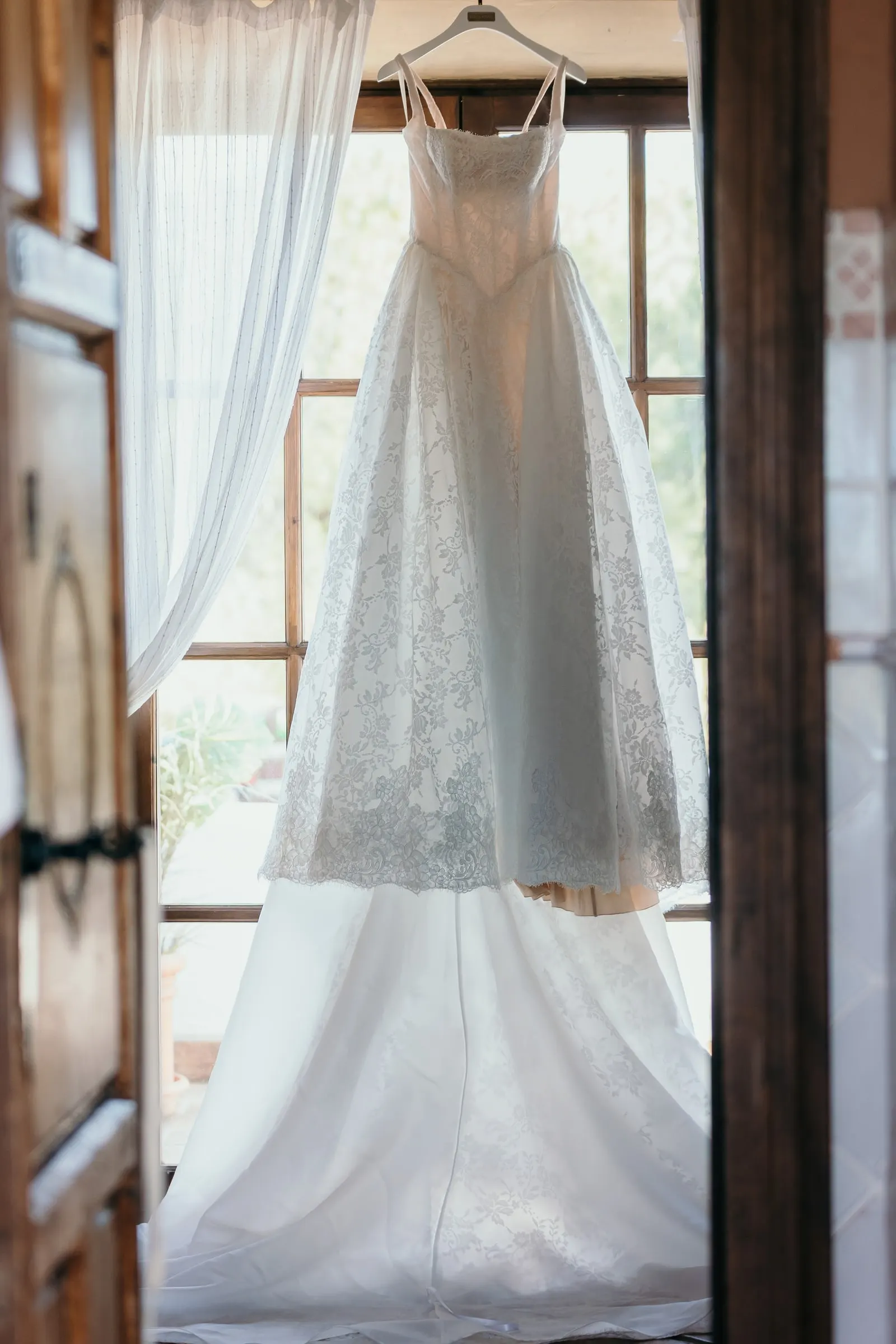 The wedding dress hanging in a tall window with its long skirt reaching the floor, Hacienda San José, Mijas
