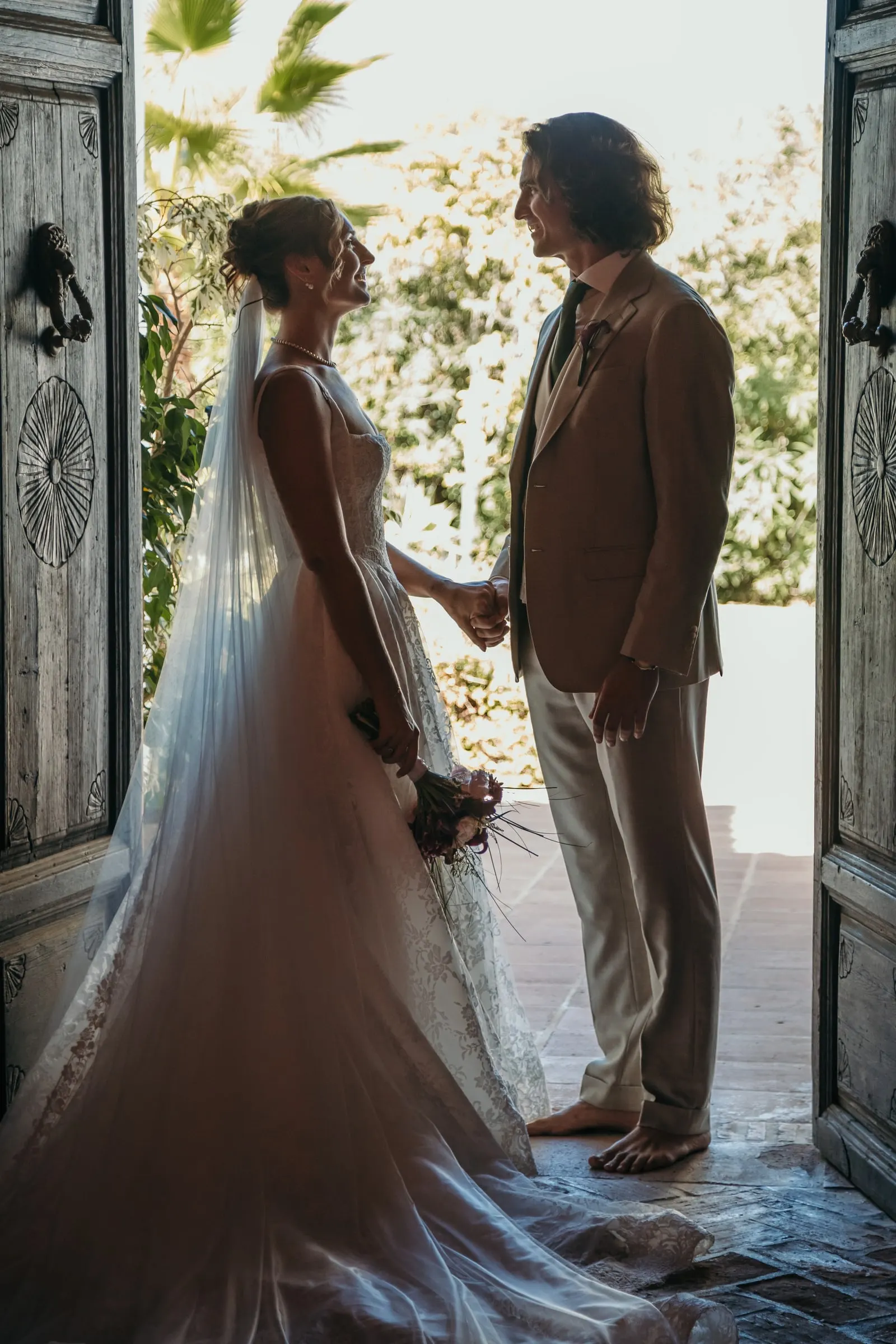 Bride and groom holding hands in an open wooden doorway against the light, Hacienda San José, Mijas