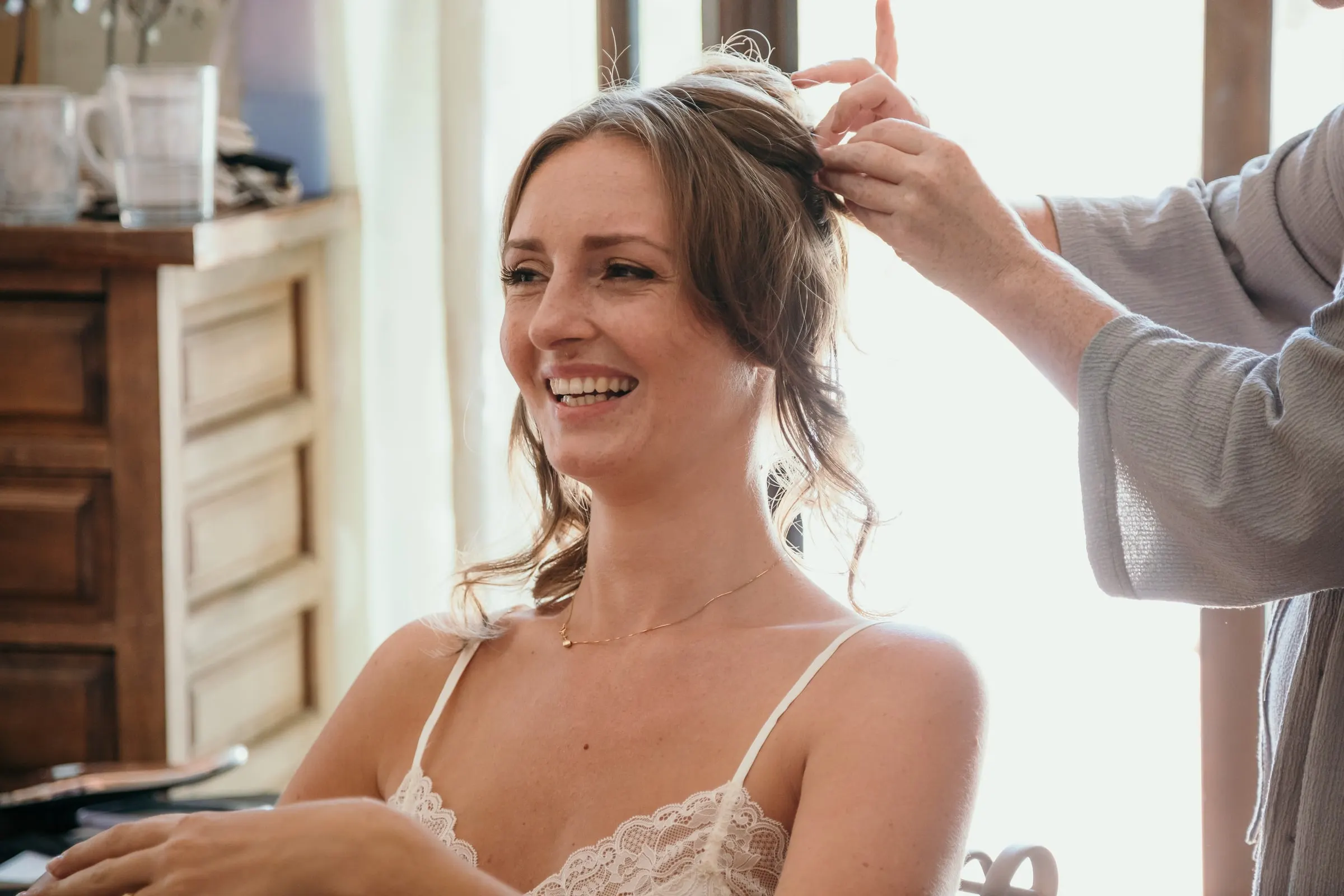 The bride laughing as a stylist pins up her hair by the window, Hacienda San José, Mijas