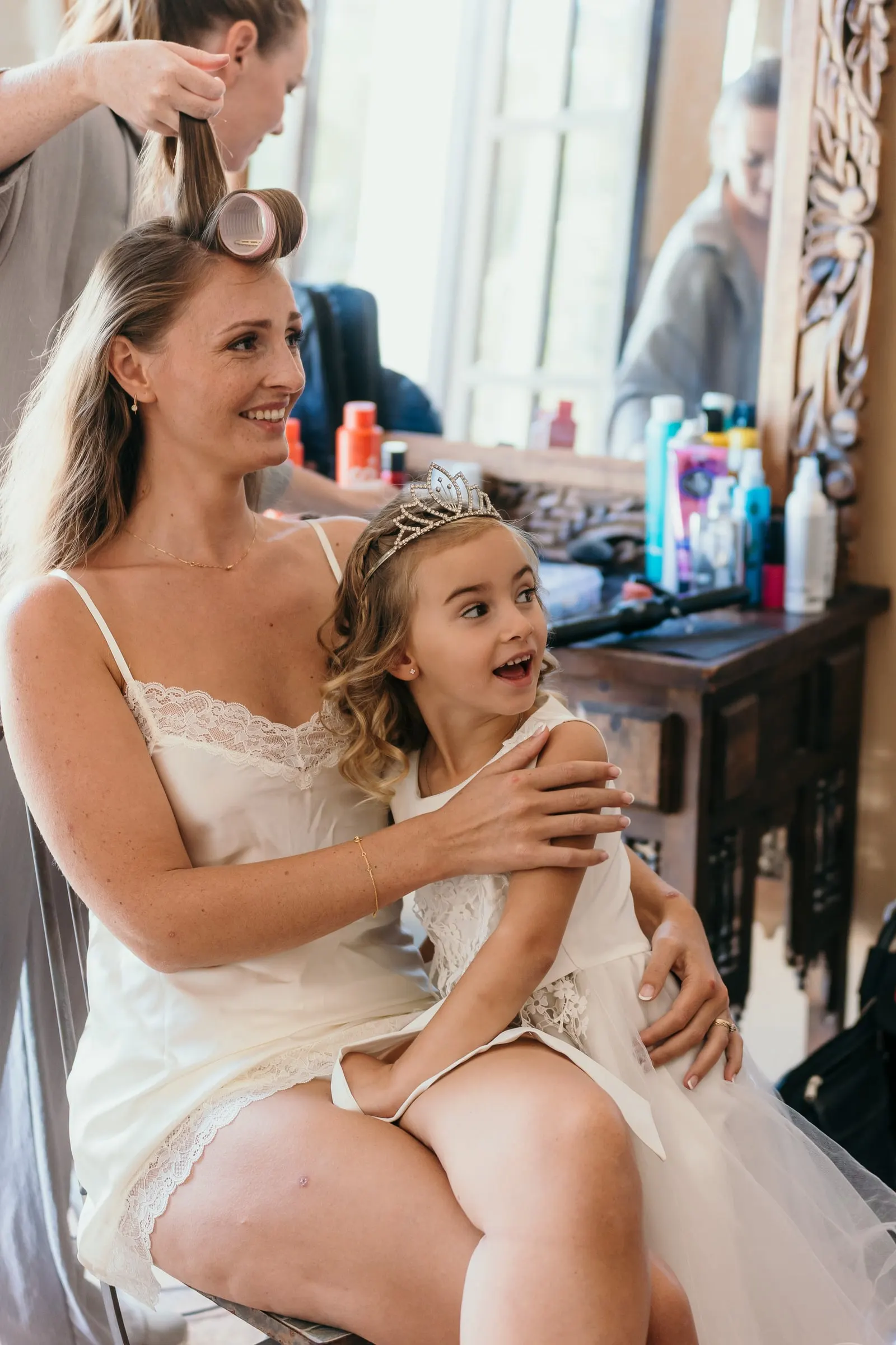 A woman in hair rollers hugging the flower girl in a tiara on her lap, Hacienda San José, Mijas