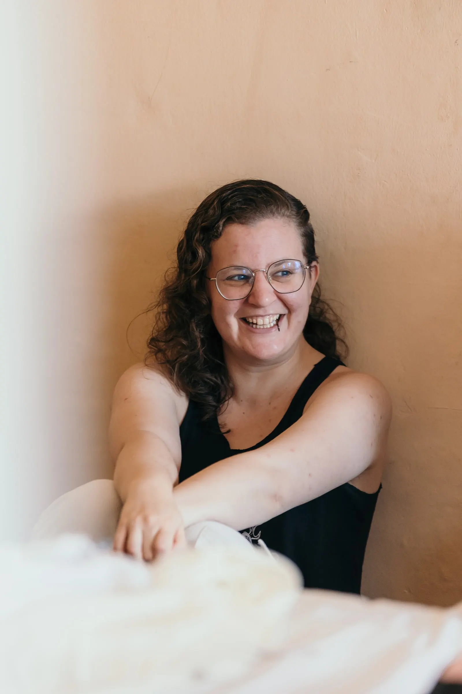 Smiling woman in glasses sitting against a warm-toned wall during the preparations at Hacienda San José, Mijas