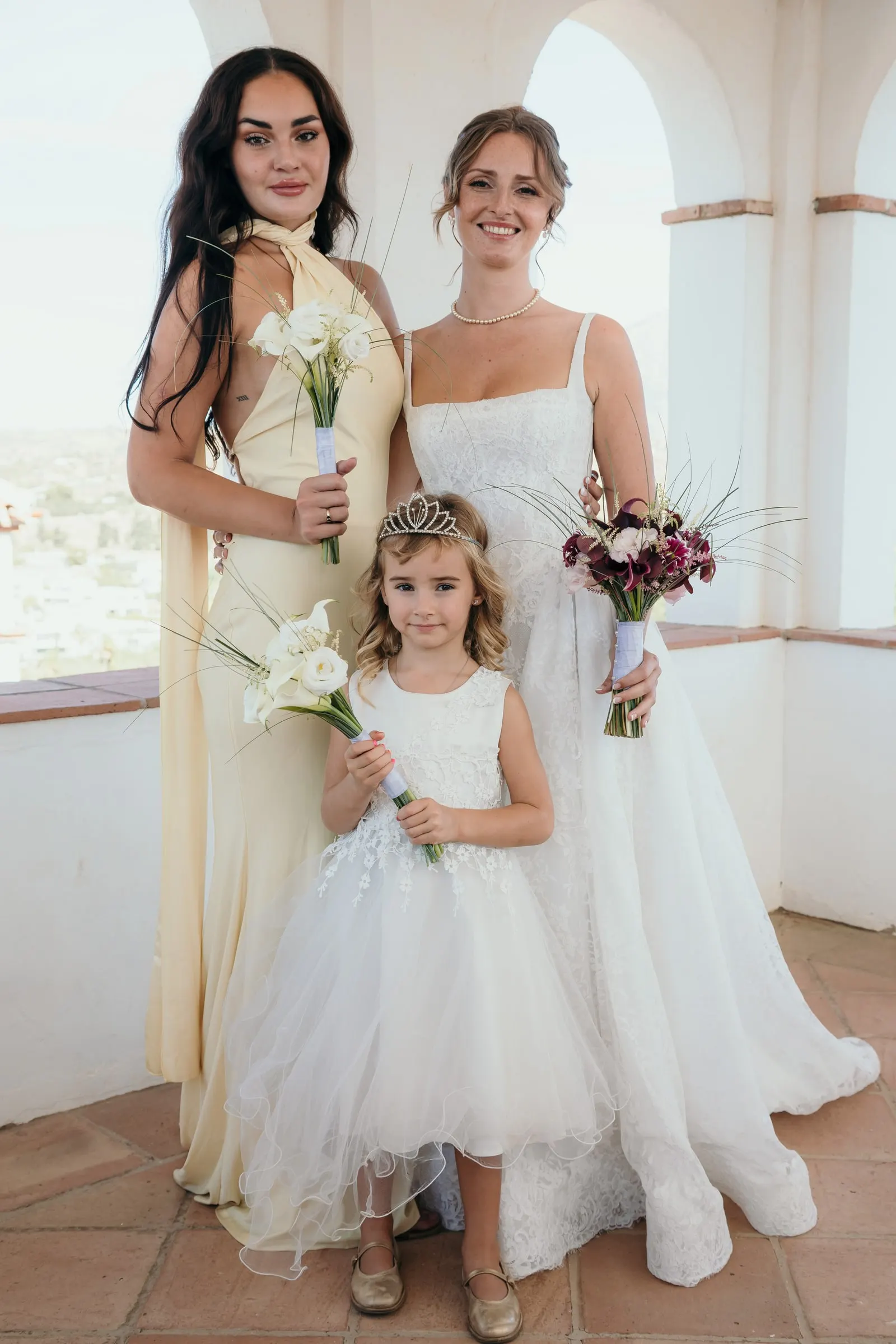 The bride with a bridesmaid in pale yellow and the flower girl in a white arched room, Hacienda San José, Mijas