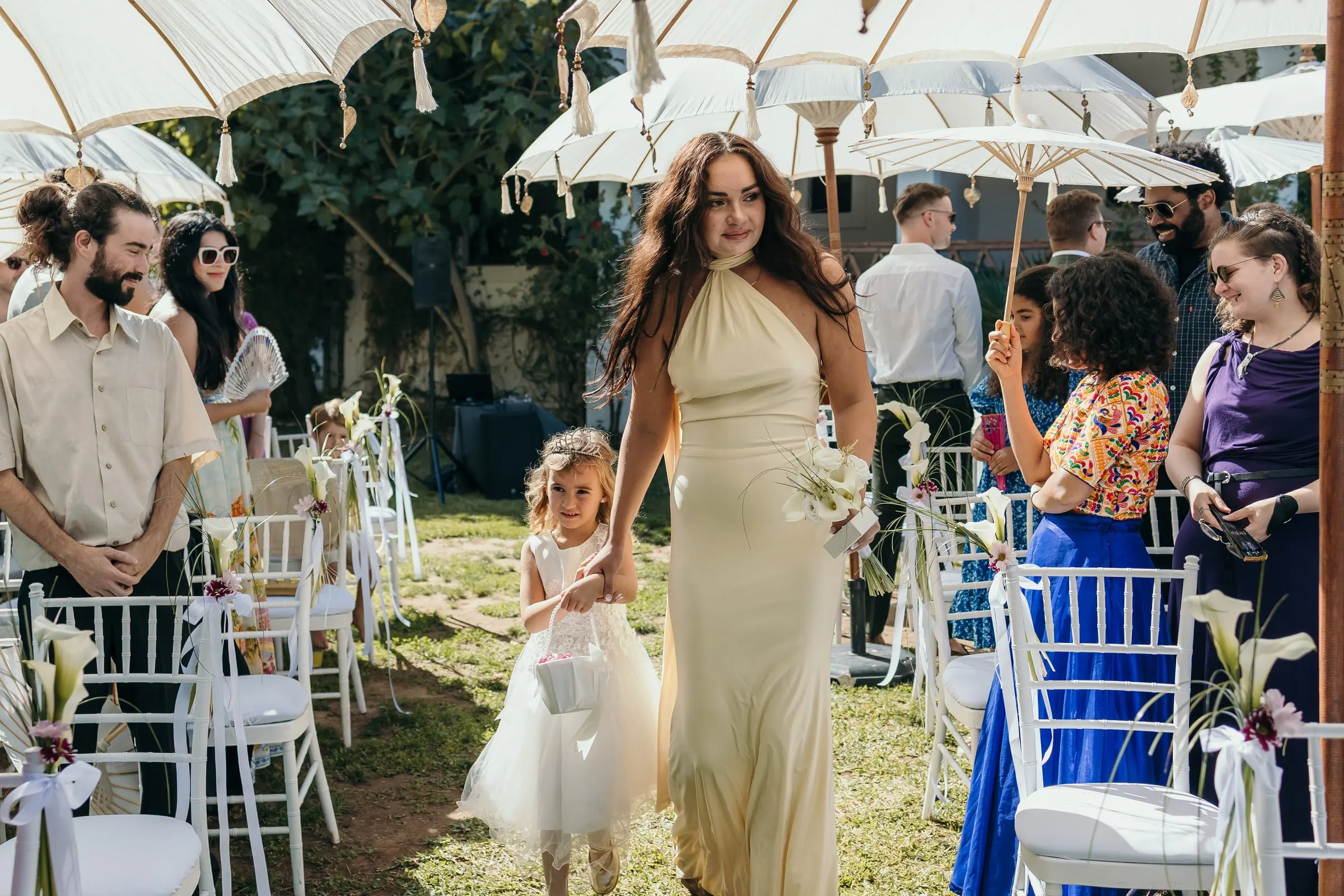 A bridesmaid in pale yellow and the flower girl walking down the aisle under parasols, Hacienda San José, Mijas