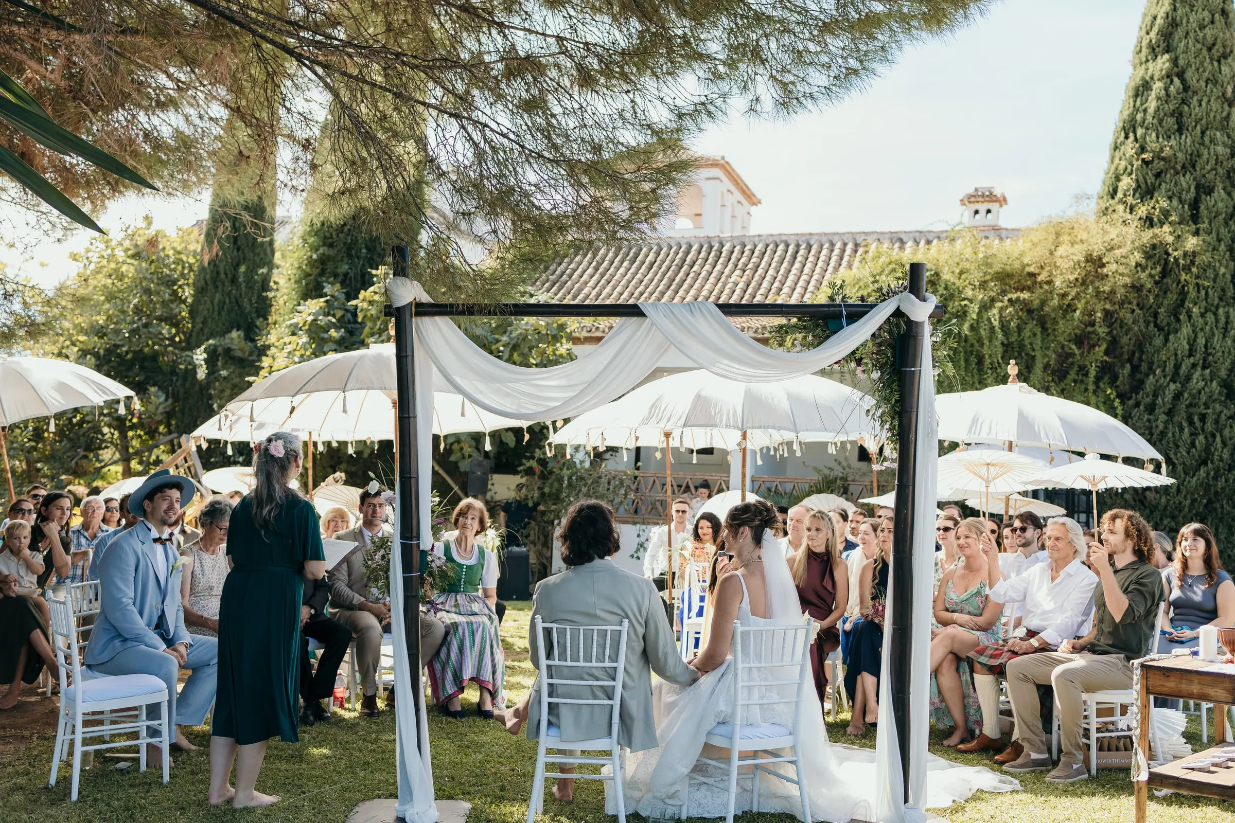 The garden ceremony from behind the guests, the couple under a draped arch, Hacienda San José, Mijas