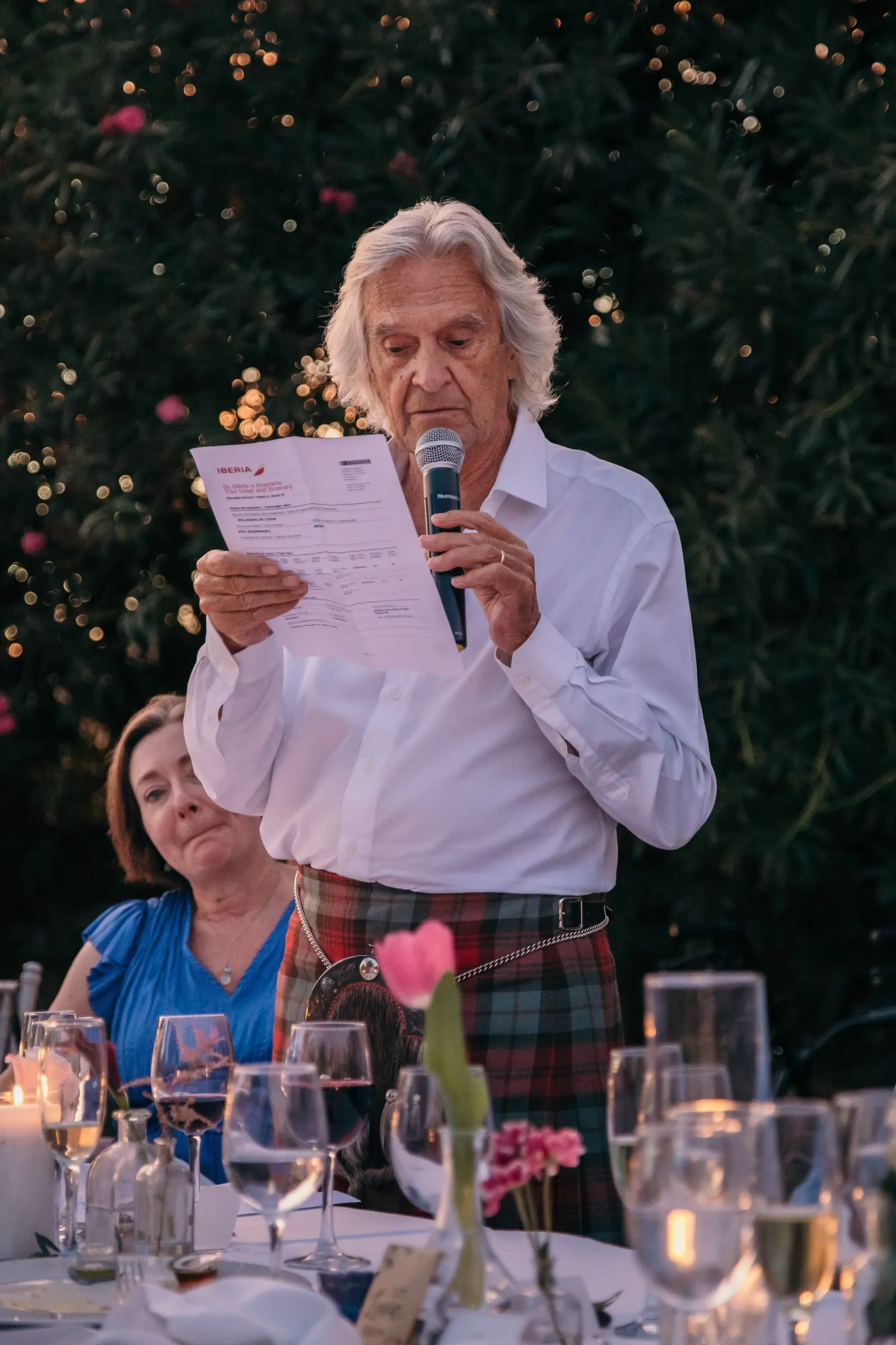 Older guest in a kilt reading a speech with a microphone at the wedding dinner at Hacienda San José, Mijas