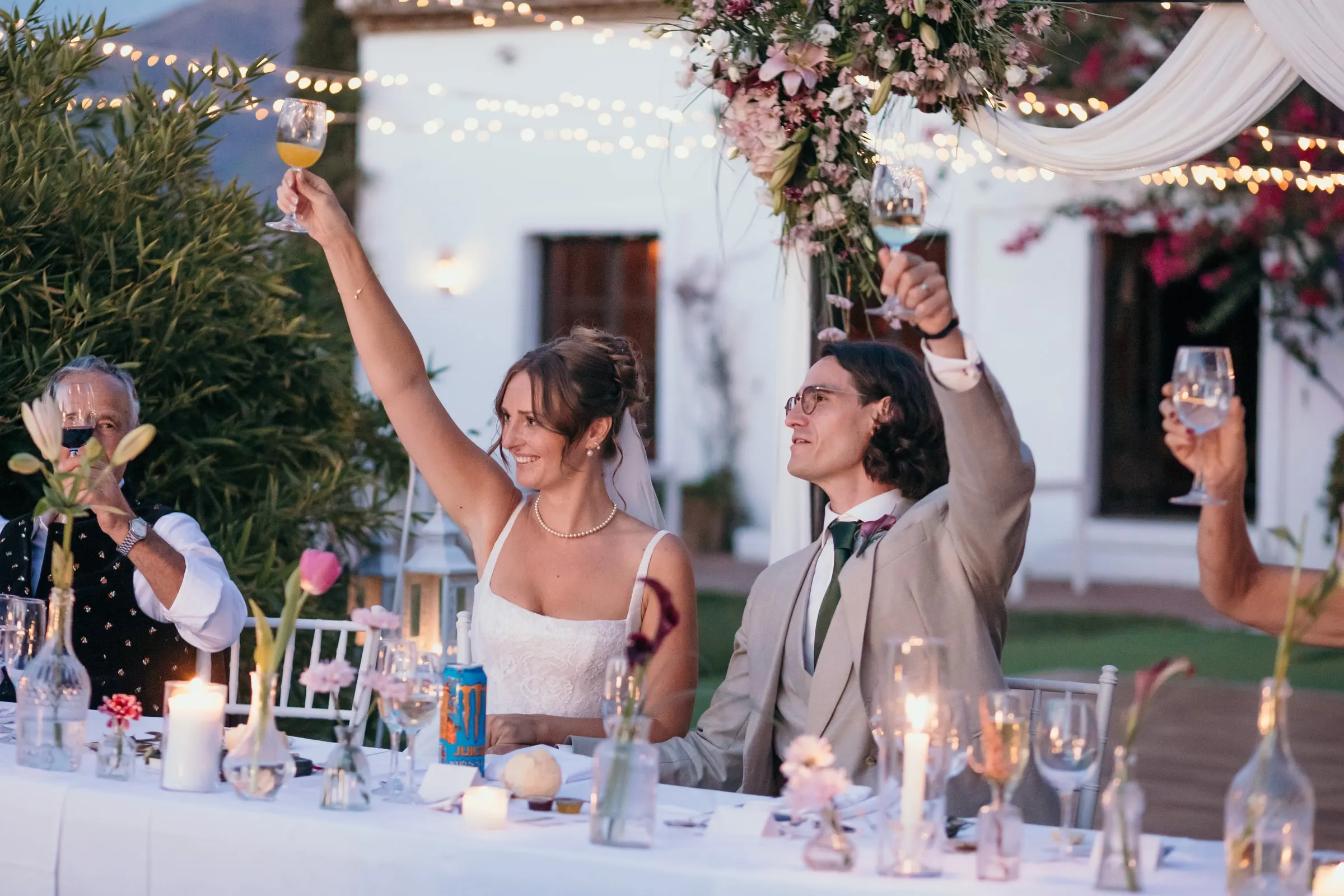 Bride and groom raising their glasses at the head table under festoon lights at Hacienda San José, Mijas