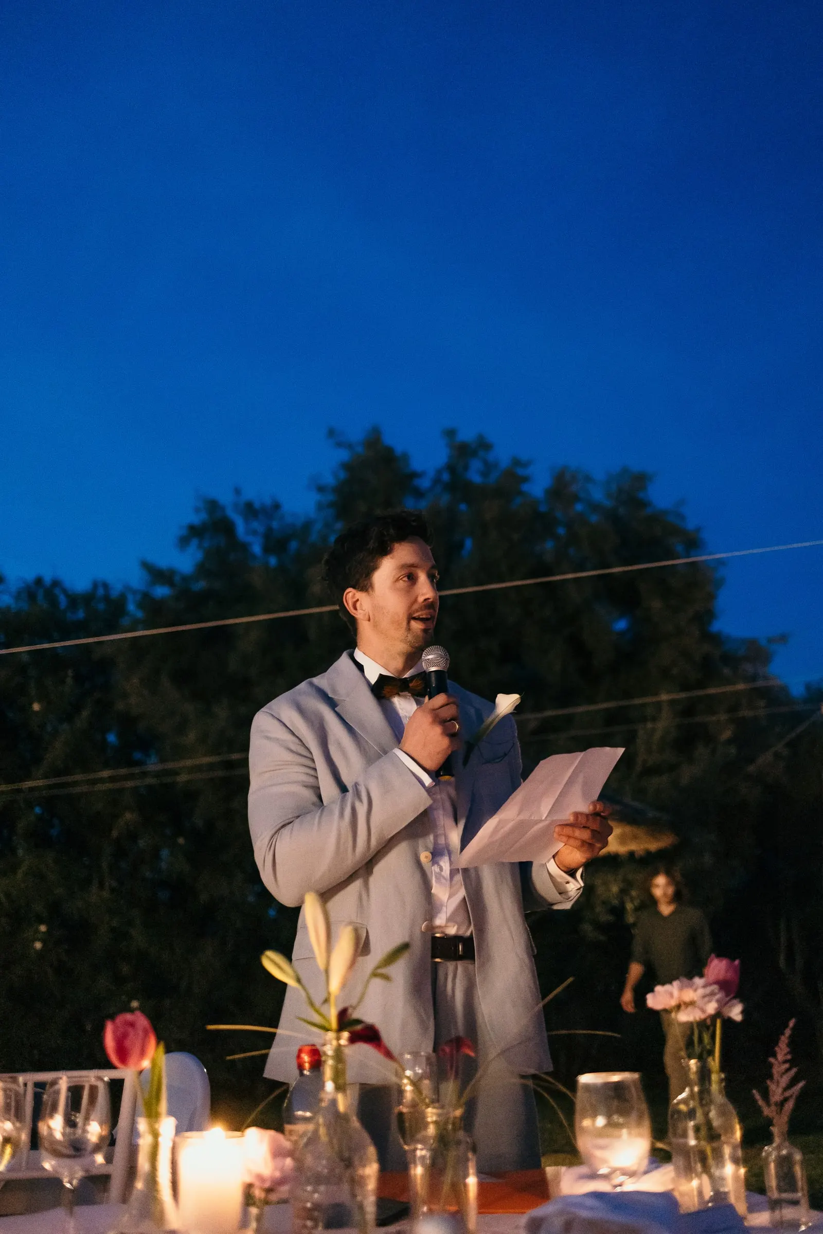 Guest in a bow tie giving a speech with a microphone against the blue evening sky at Hacienda San José, Mijas