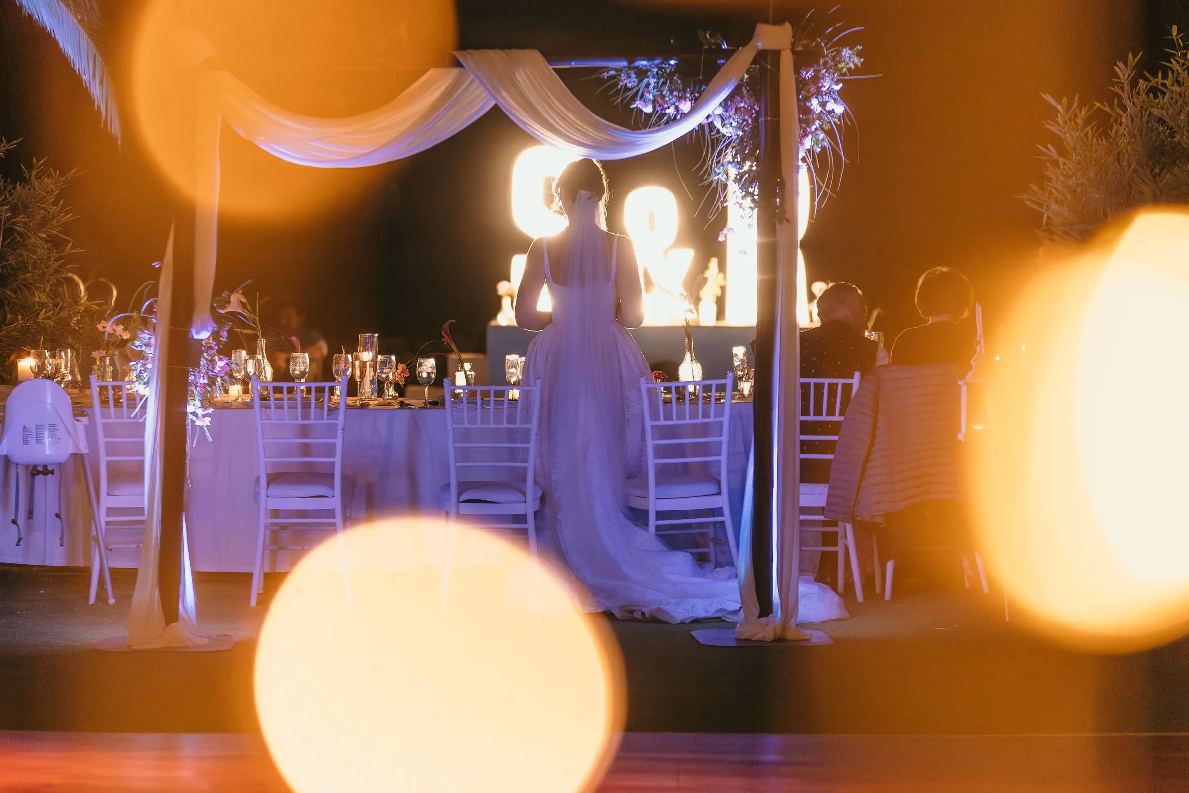 Bride seen through warm bokeh lights beside the decorated table and light-up letters at Hacienda San José, Mijas