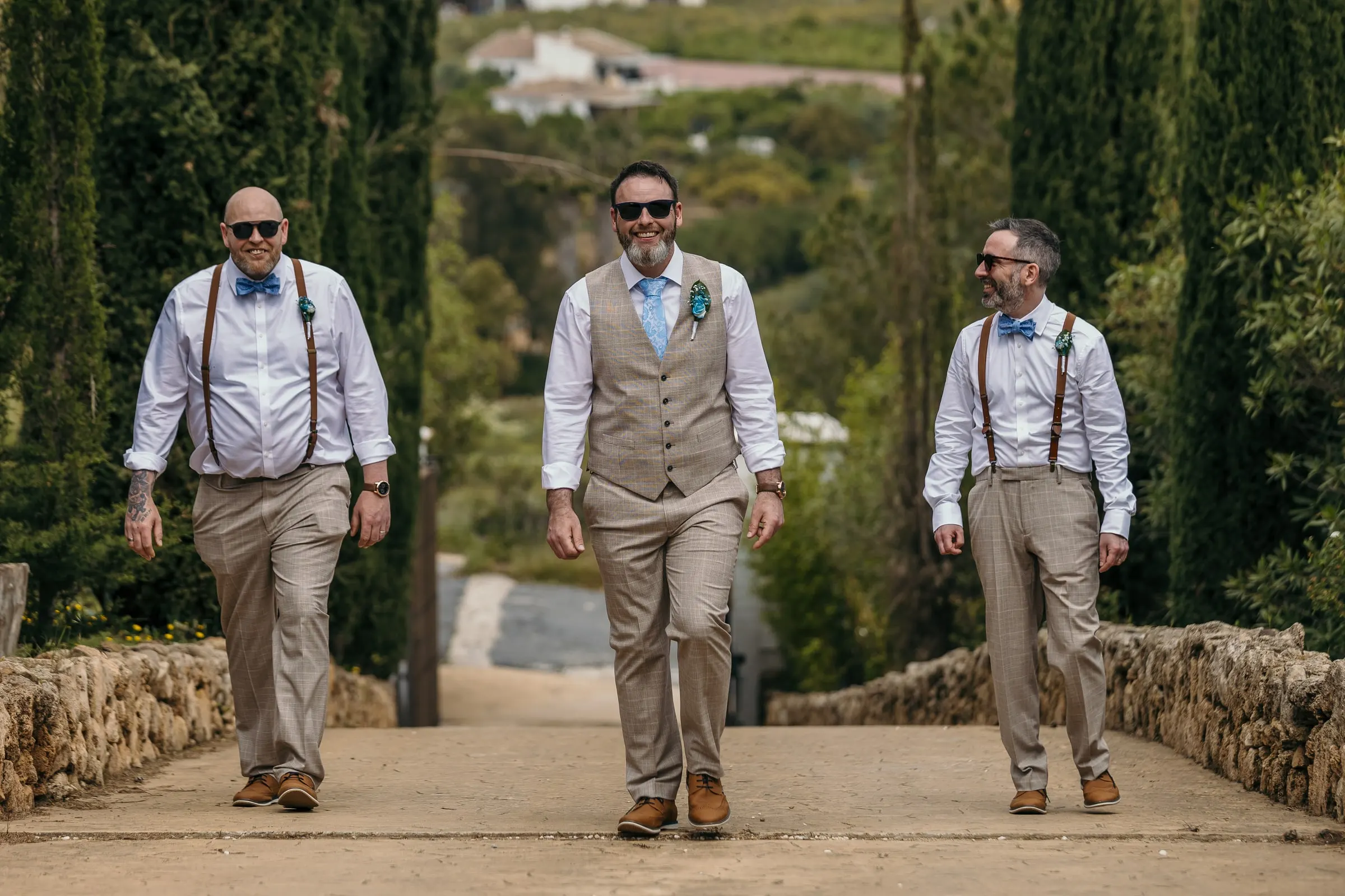 Groom and his friends in sunglasses walking up the cypress avenue at Hacienda San José