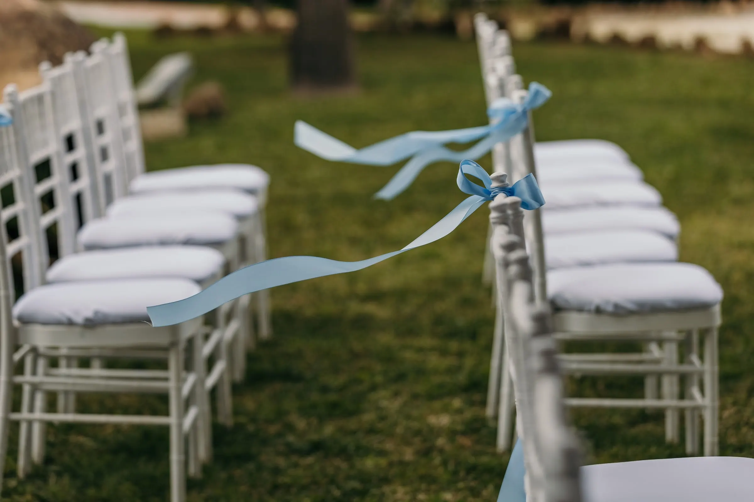 White ceremony chairs tied with pale blue ribbons on the lawn at Hacienda San José, Mijas