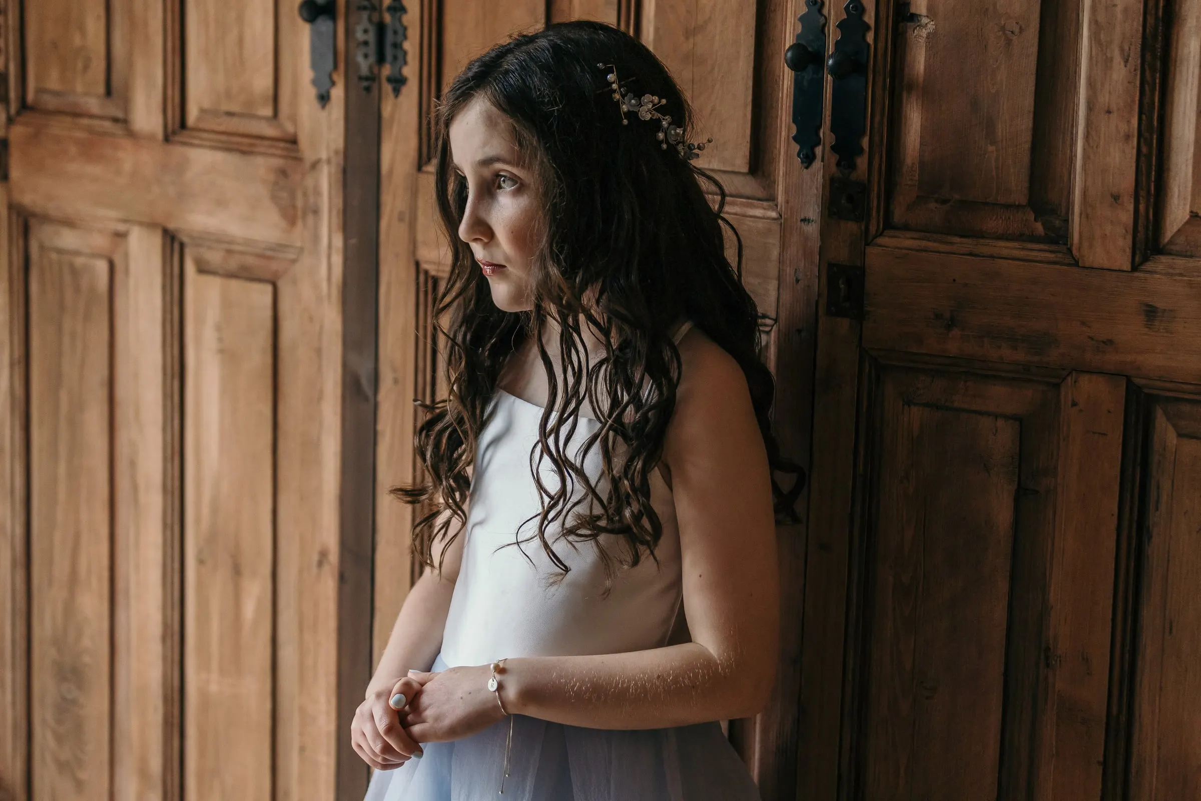 Flower girl with long curls waiting by an old wooden door at Hacienda San José